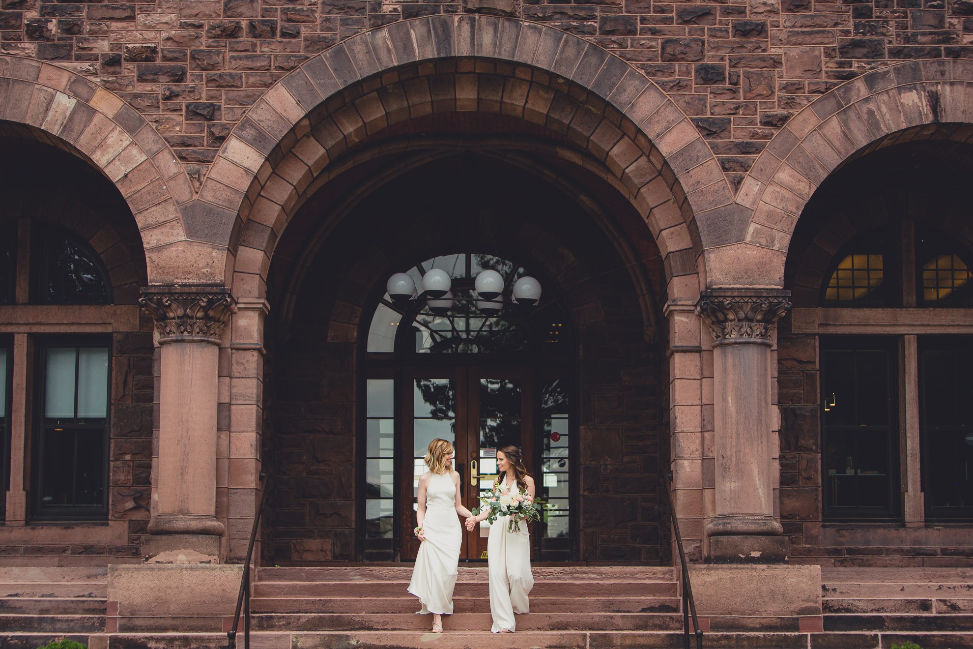 brides look at each other while walking down steps during portrait session before wedding at Hotel Henry in Buffalo, NY