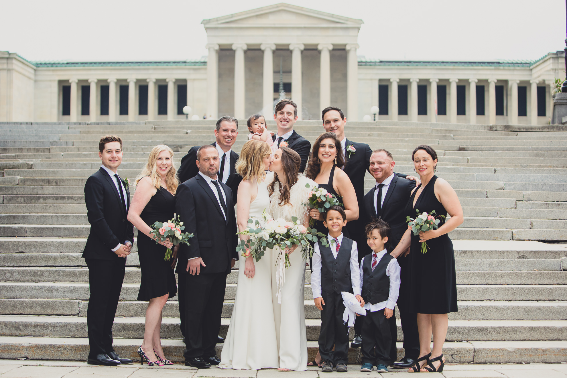 wedding party poses for portrait on steps to Hoyt Lake brides slow dance on top of steps to Hoyt Lake during portrait session on wedding day in front of Albright Knox in Delaware Park in Buffalo, NY