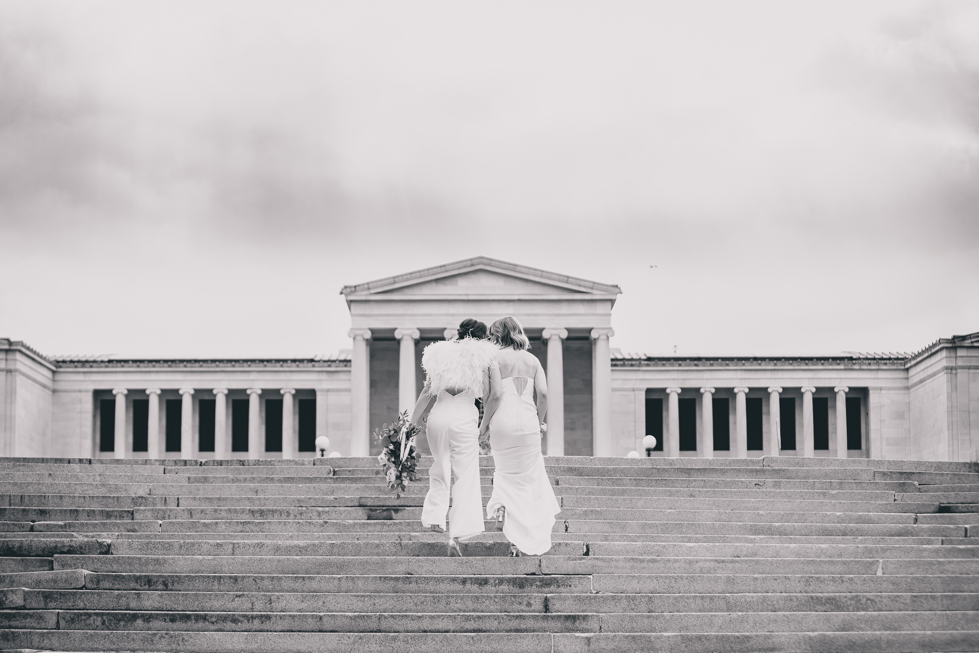 brides walk up steps to Hoyt Lake brides slow dance on top of steps to Hoyt Lake during portrait session on wedding day in front of Albright Knox in Delaware Park in Buffalo, NY