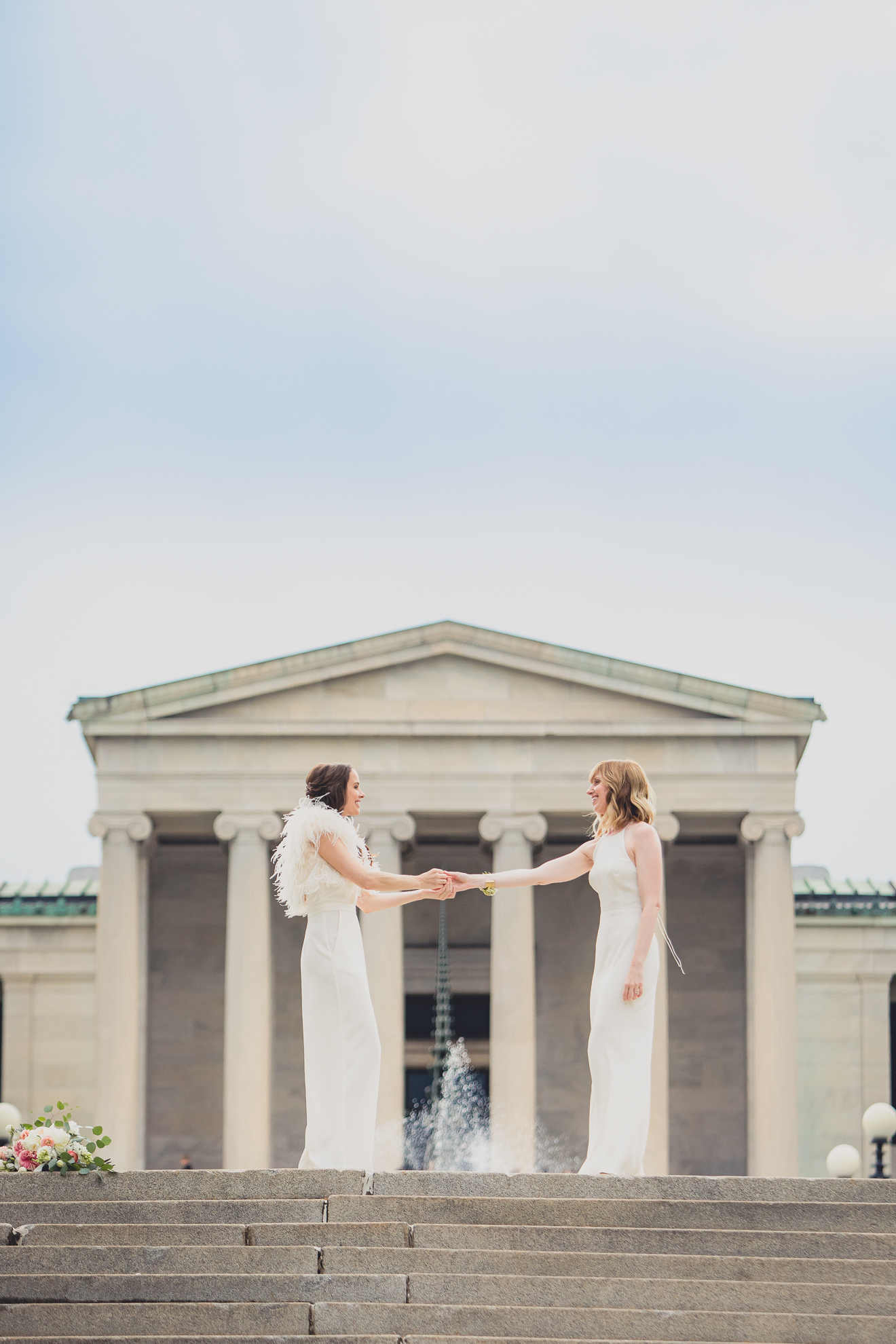 brides slow dance on top of steps to Hoyt Lake during portrait session on wedding day in front of Albright Knox in Delaware Park in Buffalo, NY