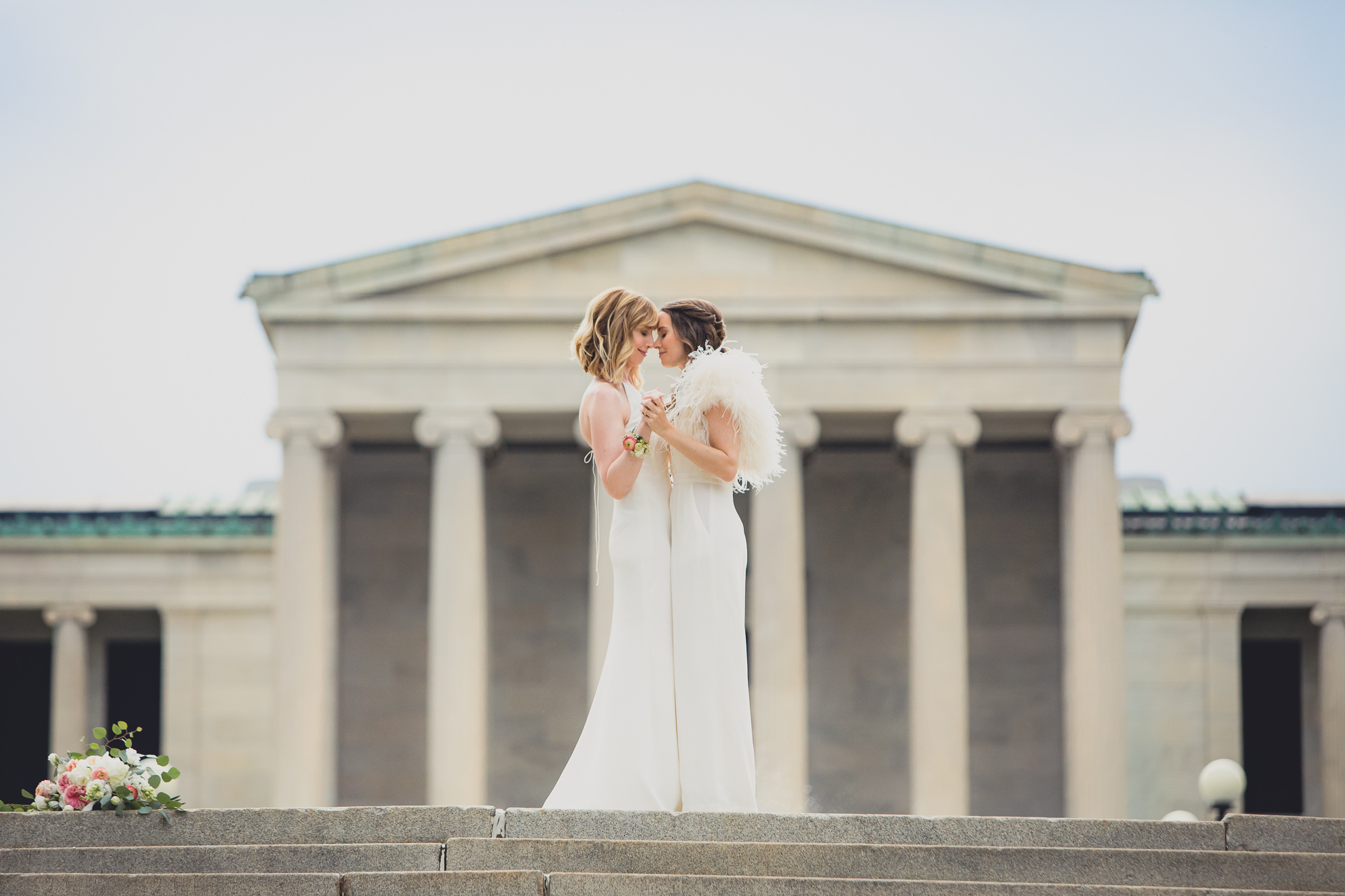 brides slow dance on top of steps to Hoyt Lake during portrait session on wedding day in front of Albright Knox in Delaware Park in Buffalo, NY