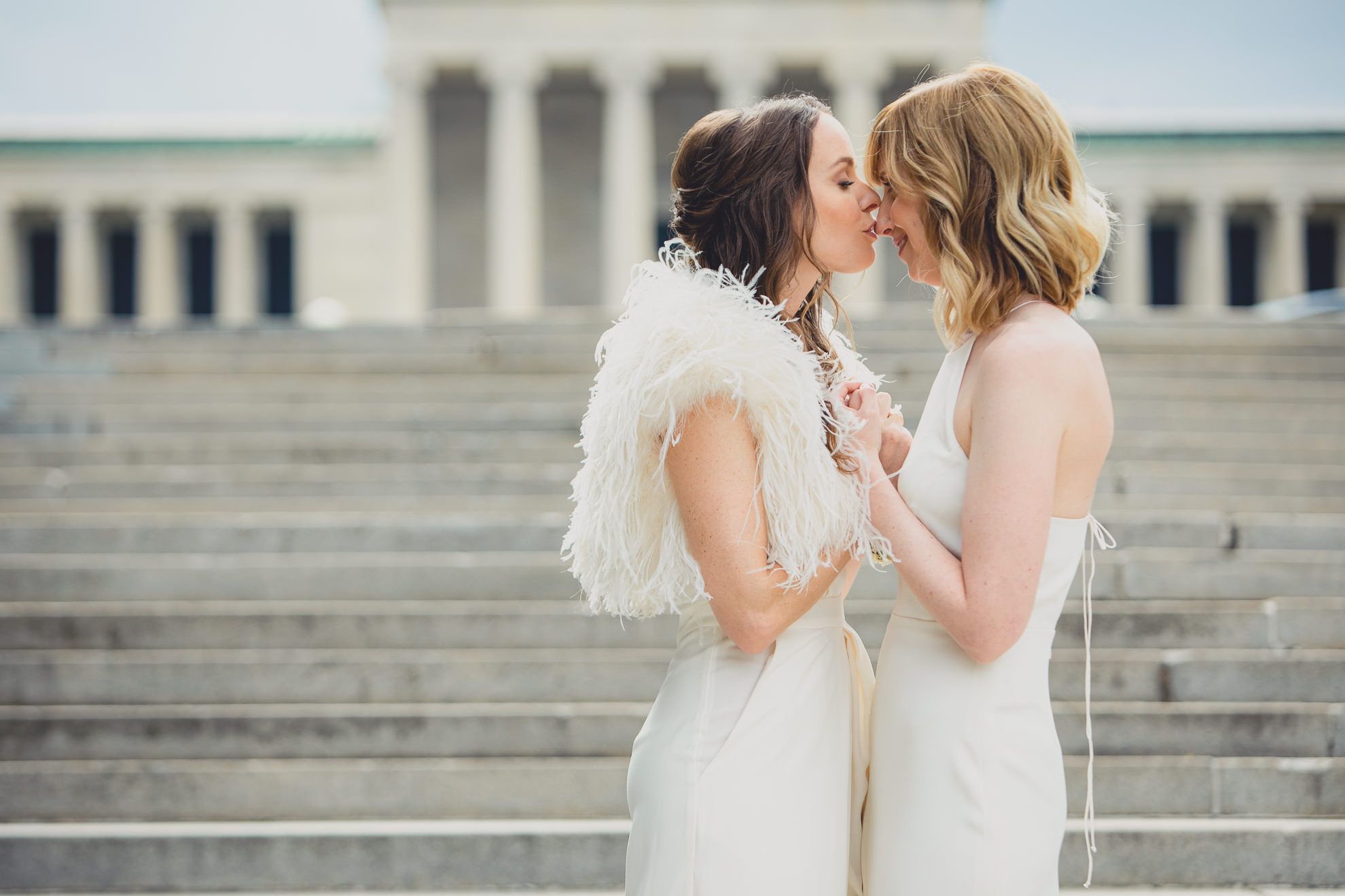 bride kisses bride on nose during portrait session on wedding day in front of Albright Knox in Delaware Park in Buffalo, NY