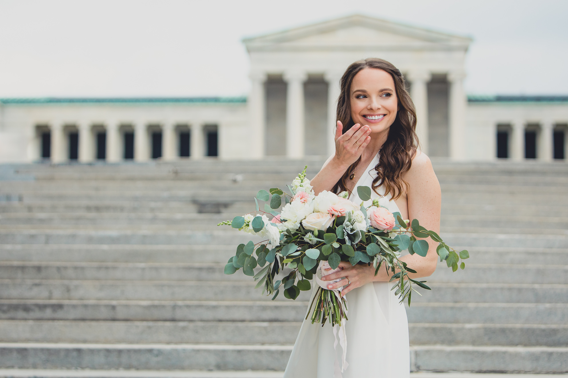 bride poses for portrait on wedding day ceremony in front of Albright Knox in Delaware Park in Buffalo, NY