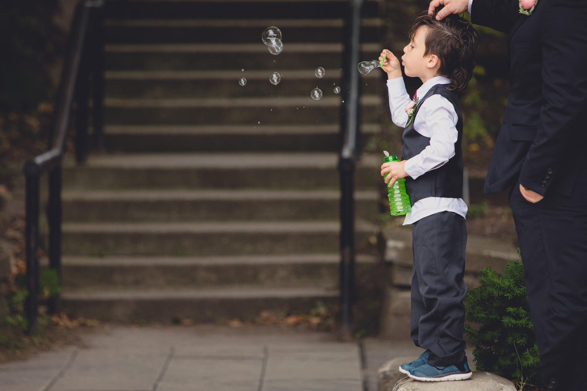 ring bearer blows bubbles during wedding ceremony in front of Hoyt Lake at Marcy Casino in Delaware Park in Buffalo, NY