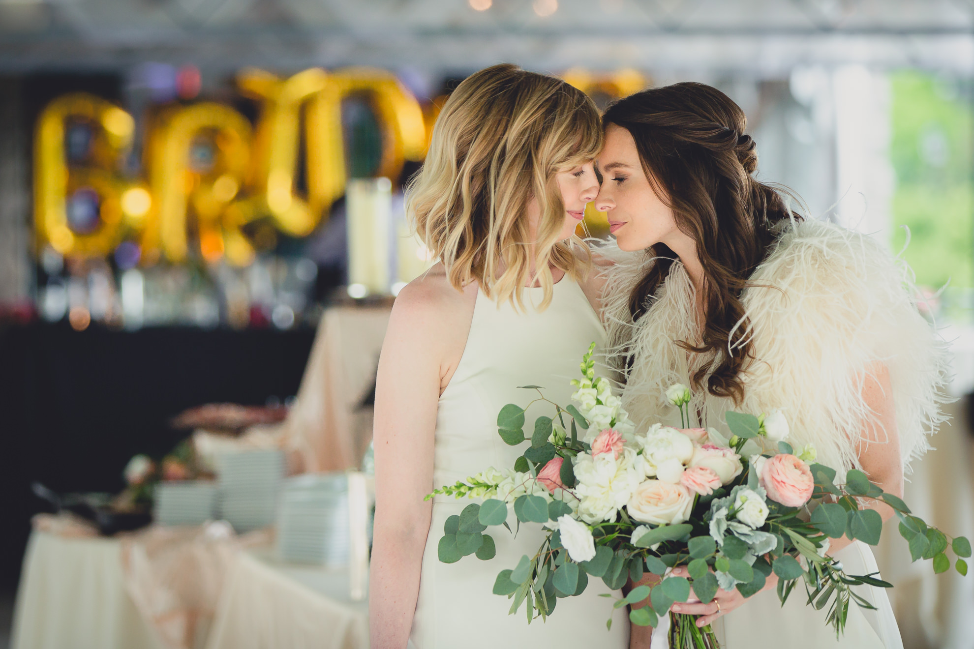 brides touch noses before walking down aisle during wedding ceremony in front of Hoyt Lake at Marcy Casino in Delaware Park in Buffalo, NY