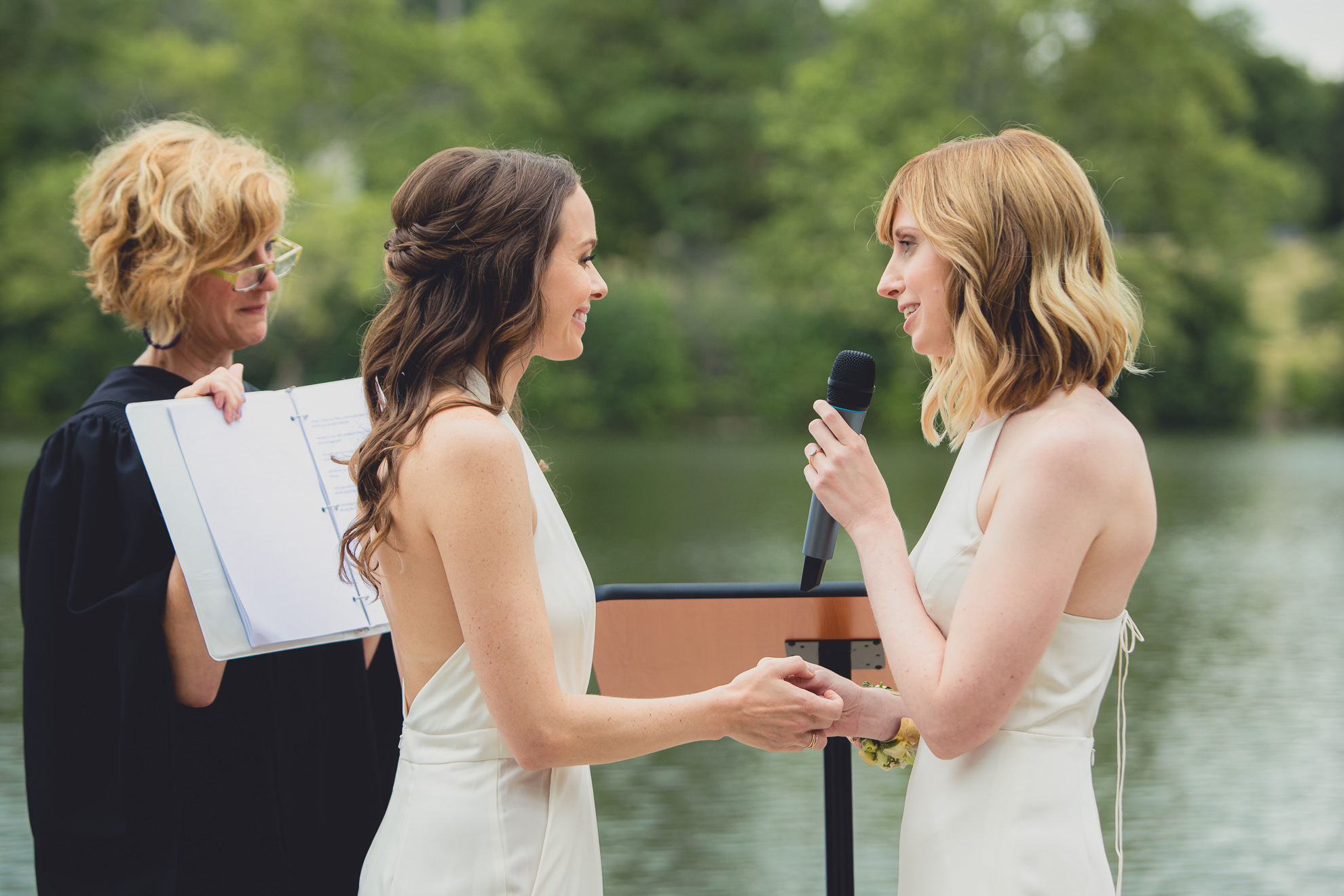 brides recite vows during wedding ceremony in front of Hoyt Lake at Marcy Casino in Delaware Park in Buffalo, NY
