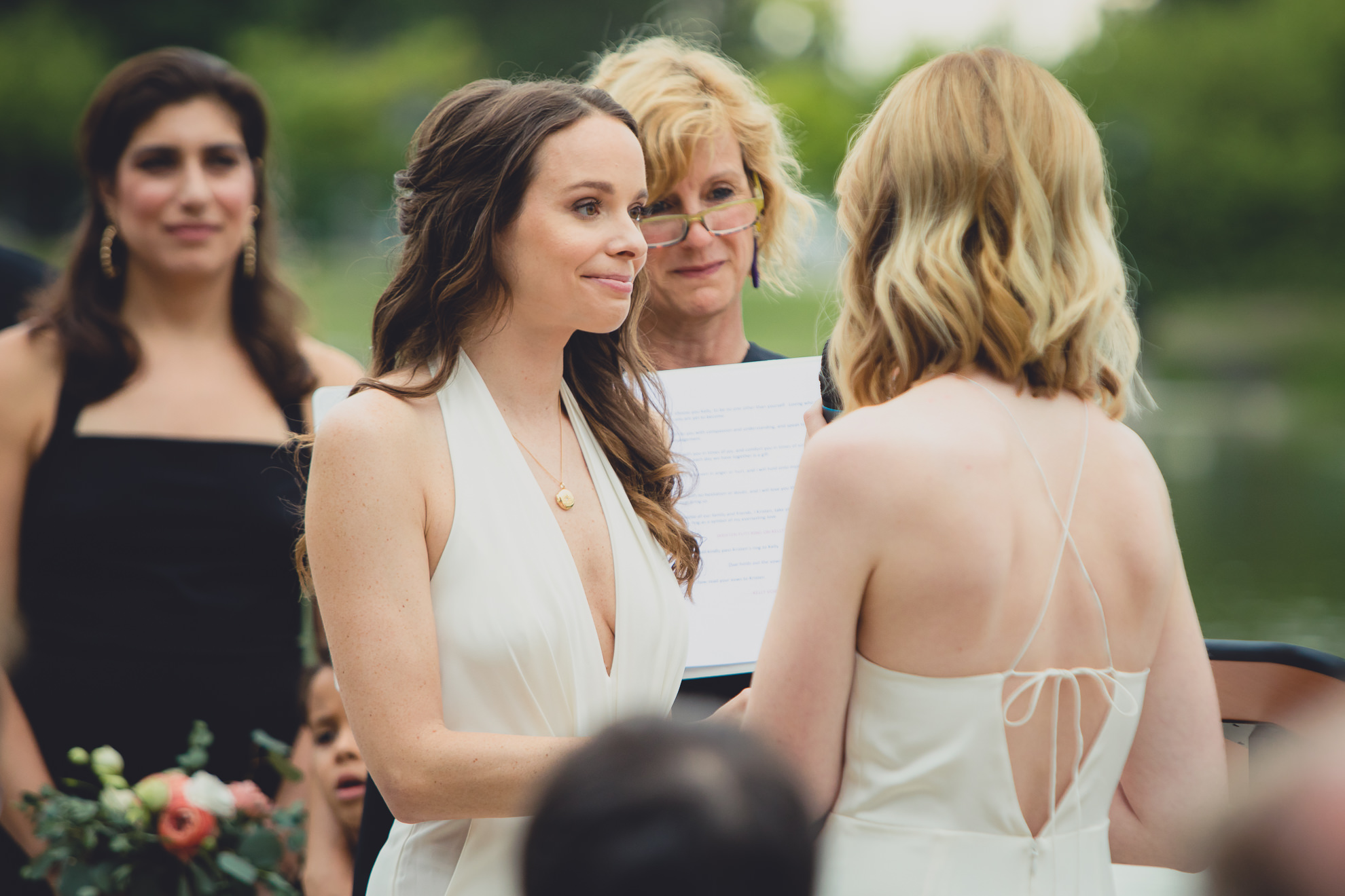 brides look at one another during wedding ceremony in front of Hoyt Lake at Marcy Casino in Delaware Park in Buffalo, NY