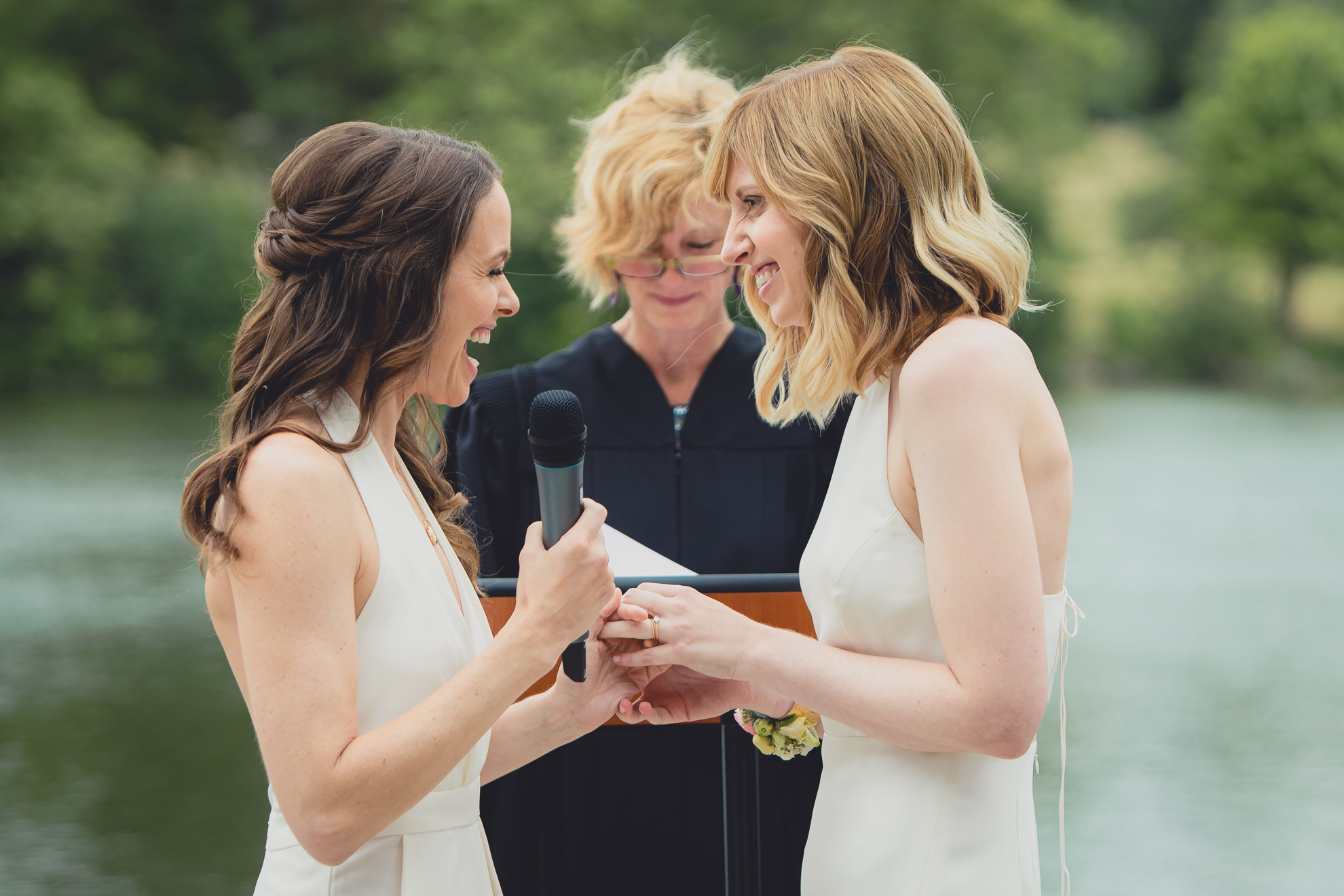brides laugh during vows during wedding ceremony in front of Hoyt Lake at Marcy Casino in Delaware Park in Buffalo, NY