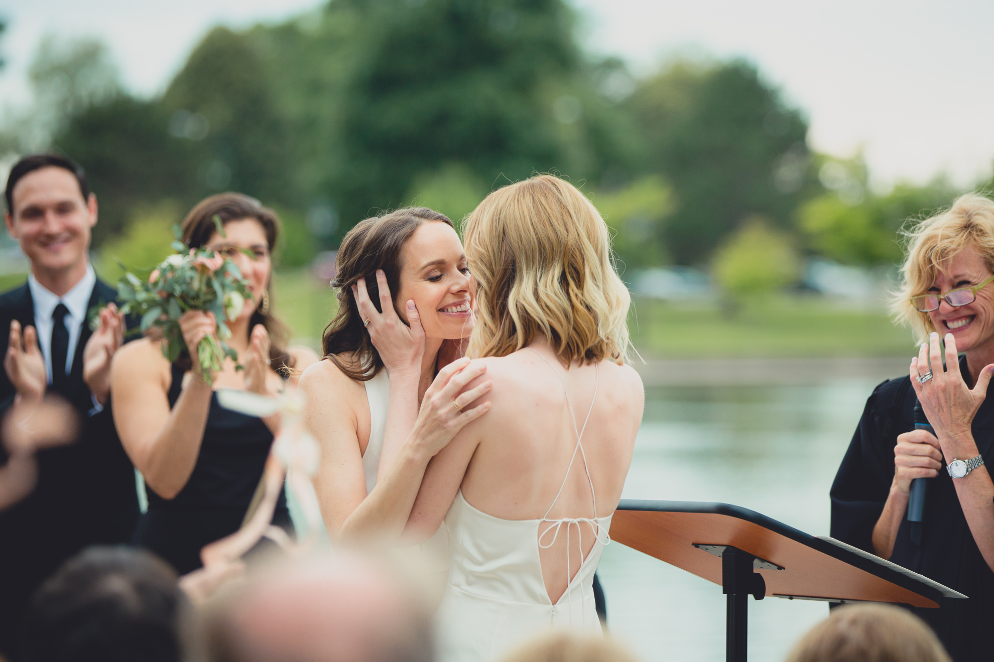 brides kiss during wedding ceremony in front of Hoyt Lake at Marcy Casino in Delaware Park in Buffalo, NY