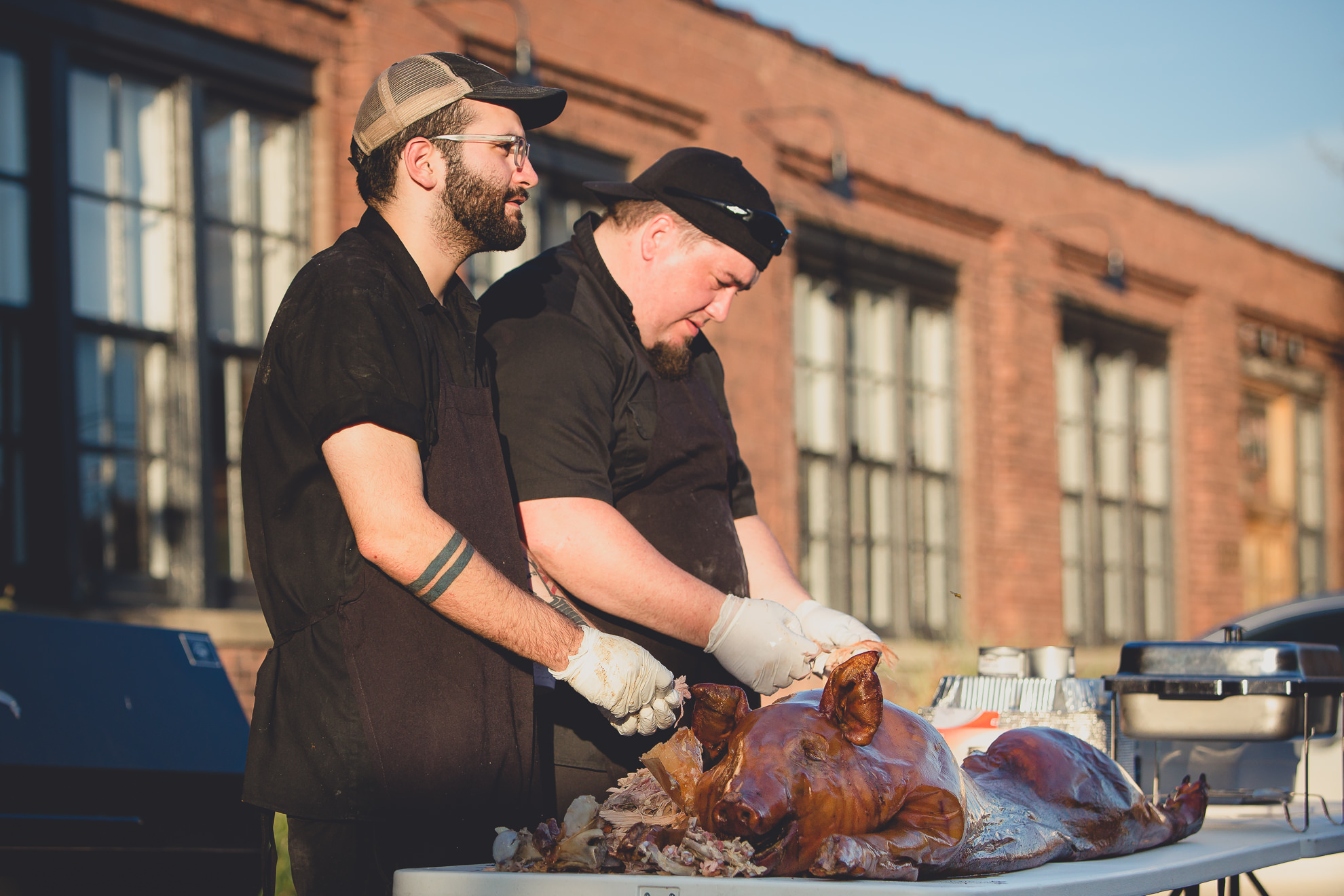 two men prepare pig roast during outdoor wedding reception at the Revelry in Rochester, NY 