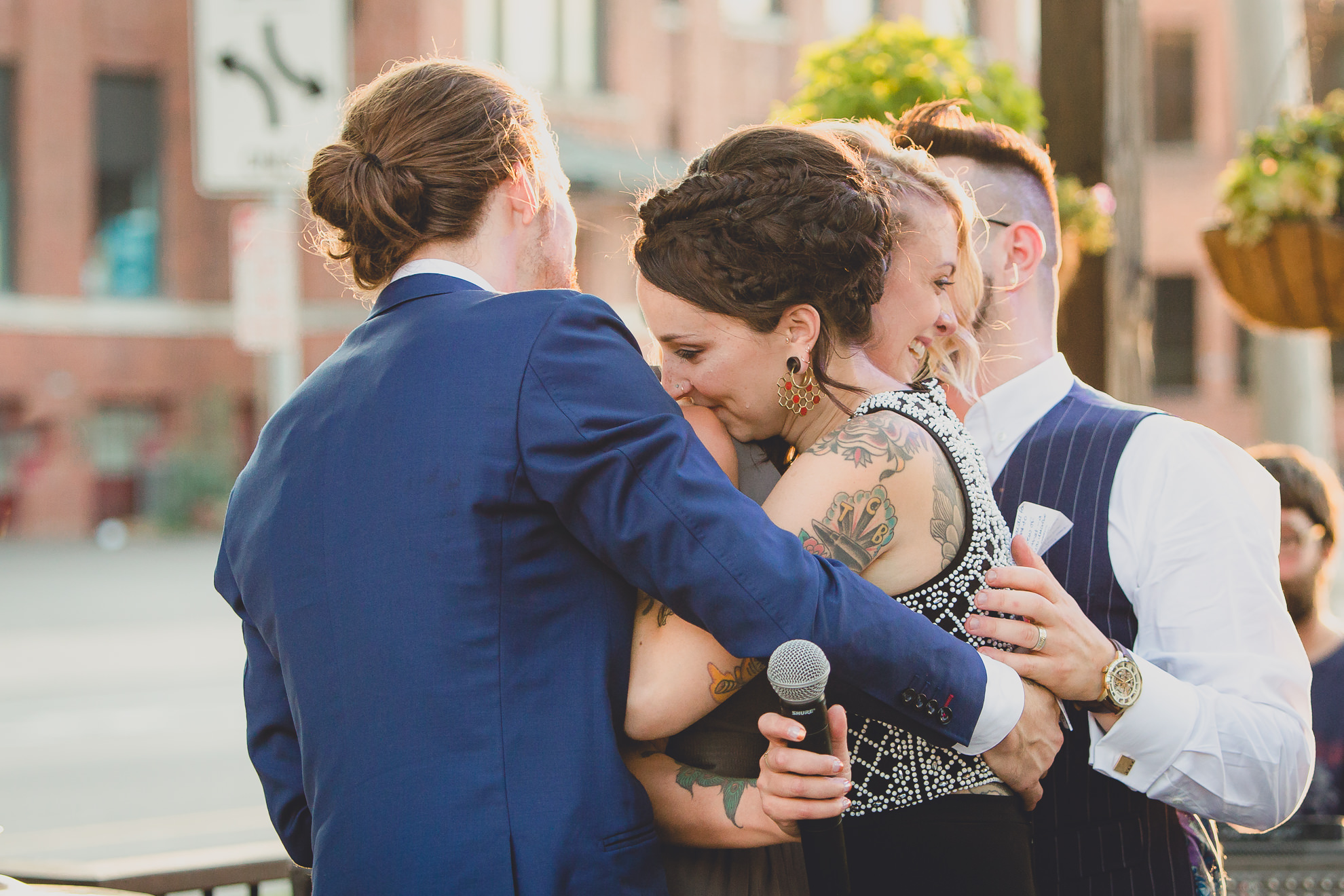 bride and groom hug best man and maid of honor after speeches during outdoor wedding reception at the Revelry in Rochester, NY 