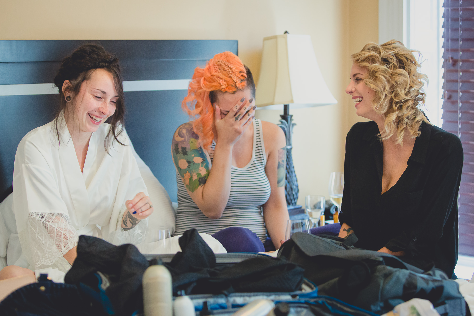 bridesmaids and bride laugh on bed  at Strathallan Hotel in Rochester, NY before wedding