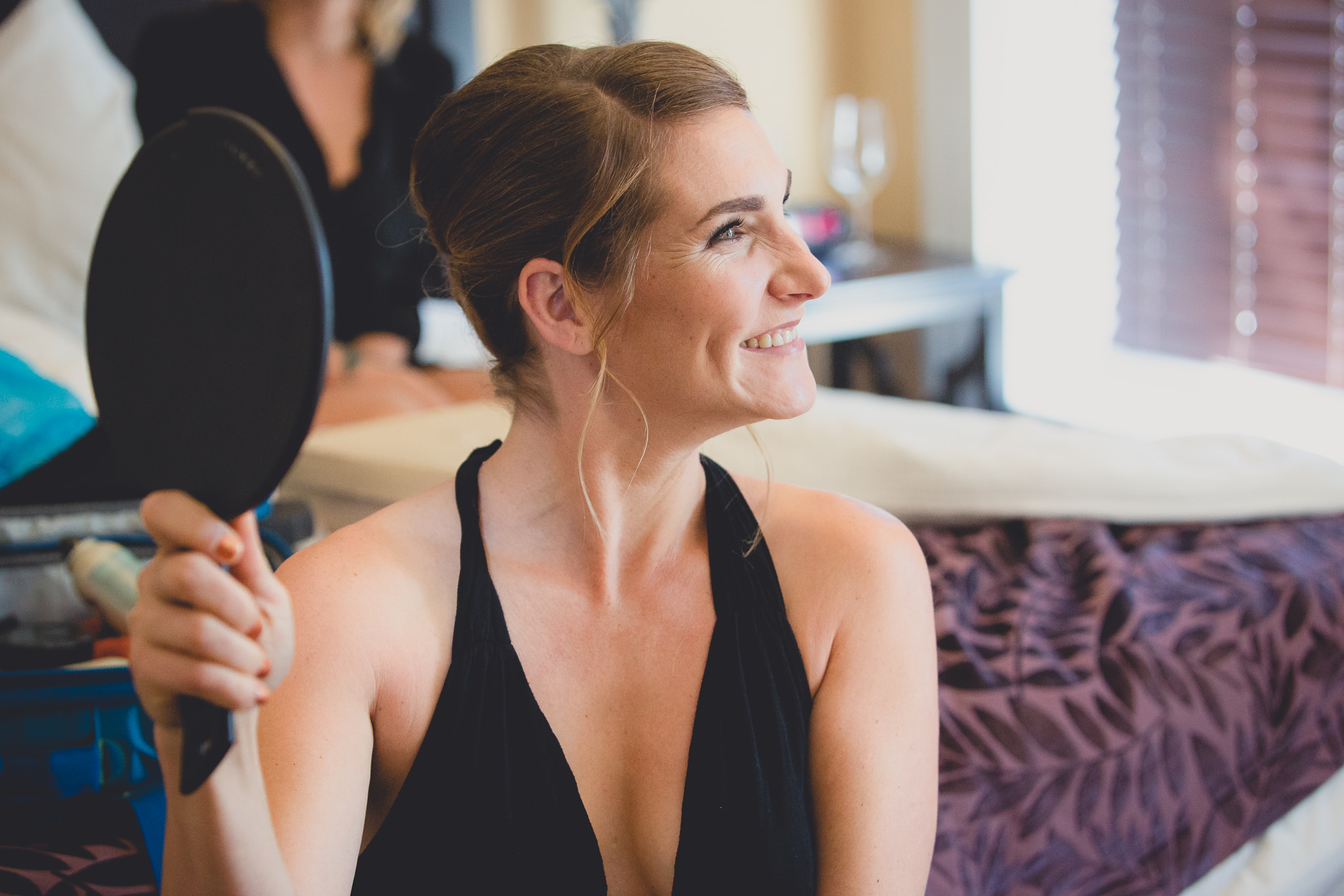 bridesmaid smiles at mirror at Strathallan Hotel in Rochester, NY before wedding