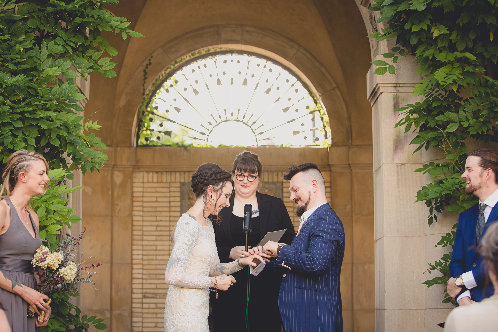 groom places ring on brides finger during garden wedding ceremony at the George Eastman House in Rochester, NY 