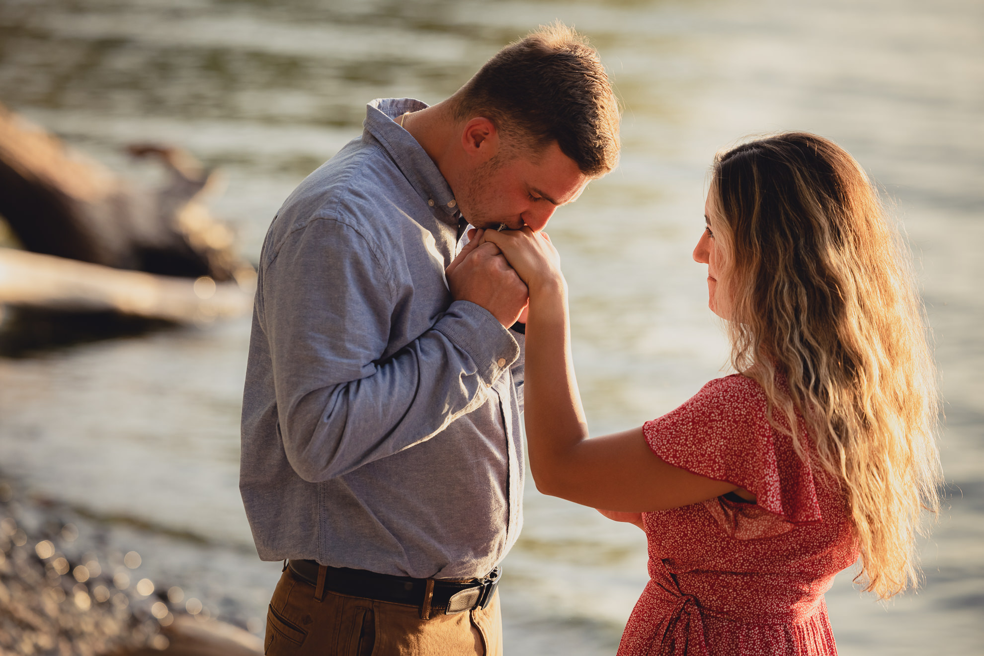 man kisses woman's ring on Lake Ontario beach at sunset during wedding engagement proposal photography in Niagara County