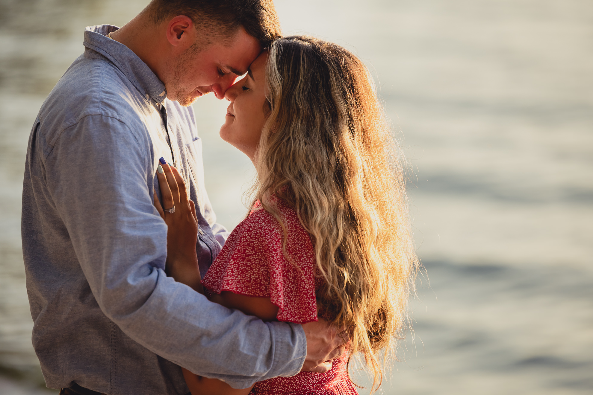 couple snuggles during proposal on Lake Ontario beach at sunset during wedding engagement proposal photography in Niagara County
