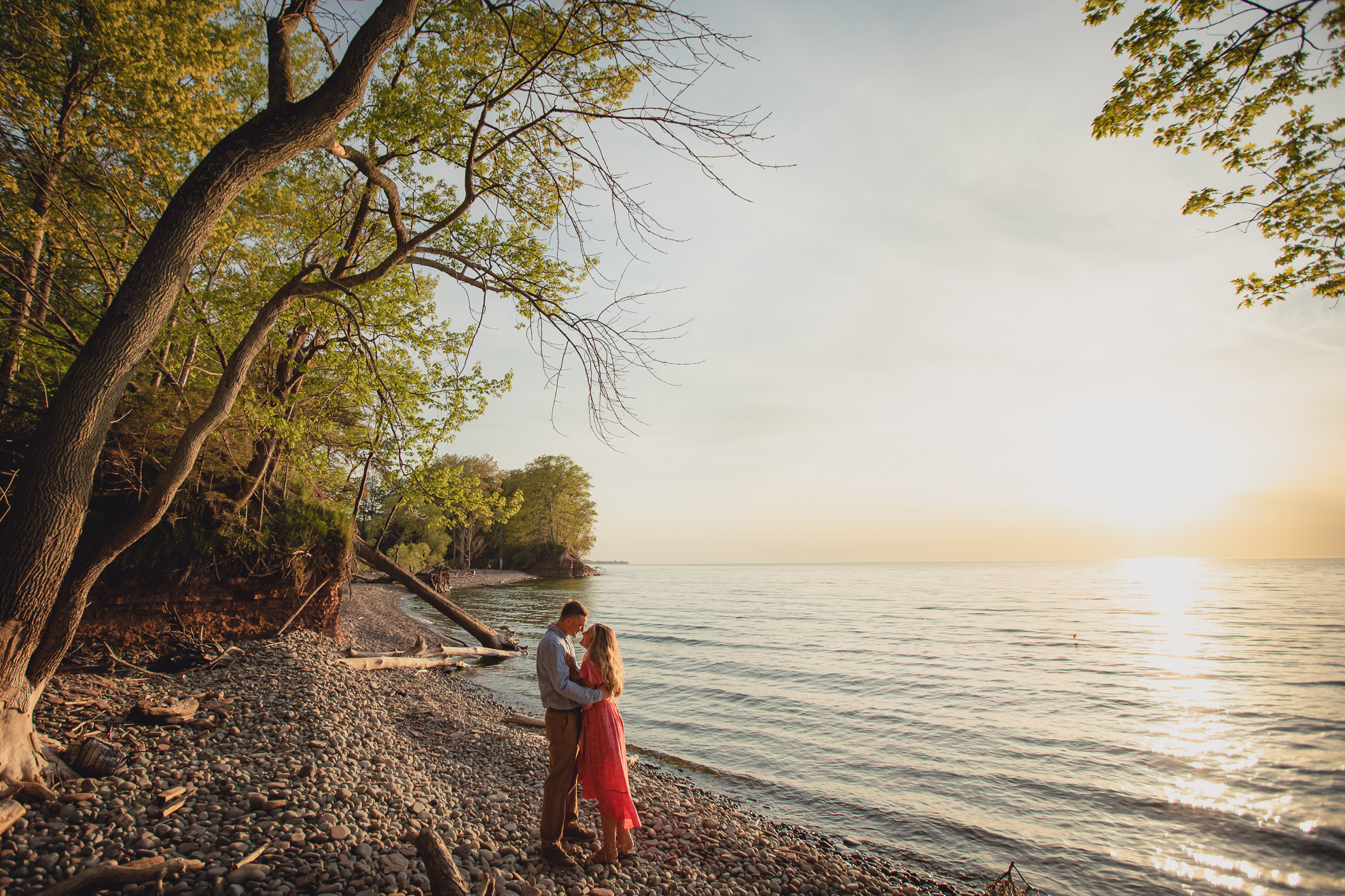 couple looks at each other during proposal on Lake Ontario beach at sunset during wedding engagement proposal photography in Niagara County