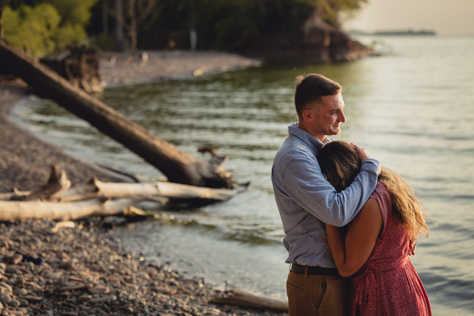 couple snuggles during proposal on Lake Ontario beach at sunset during wedding engagement proposal photography in Niagara County