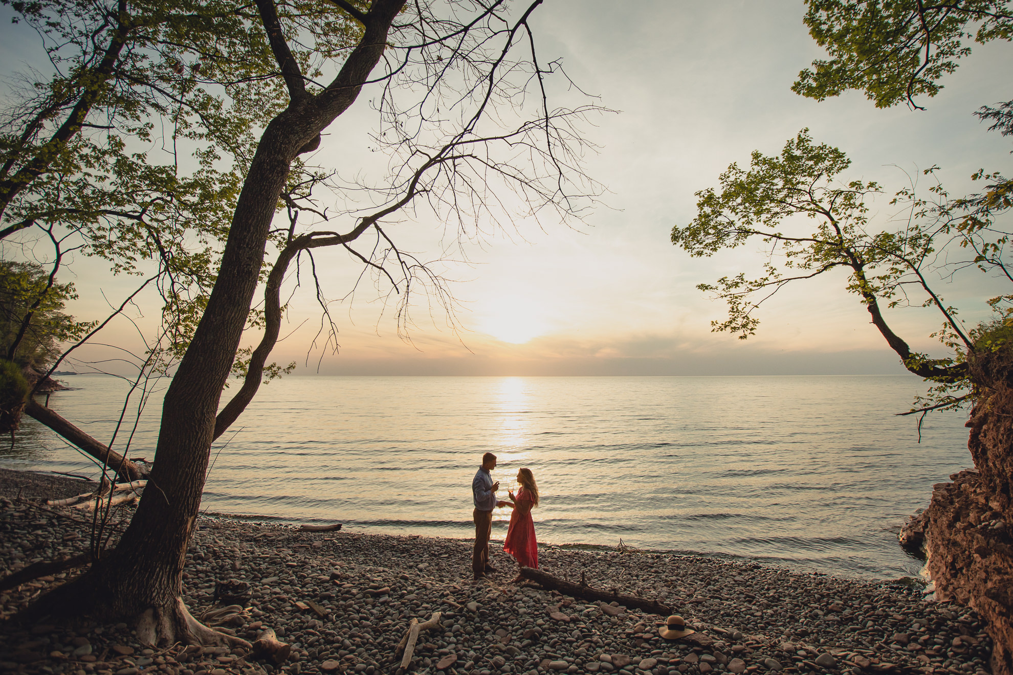 couple drinks wine after proposal on Lake Ontario beach at sunset during wedding engagement proposal photography in Niagara County