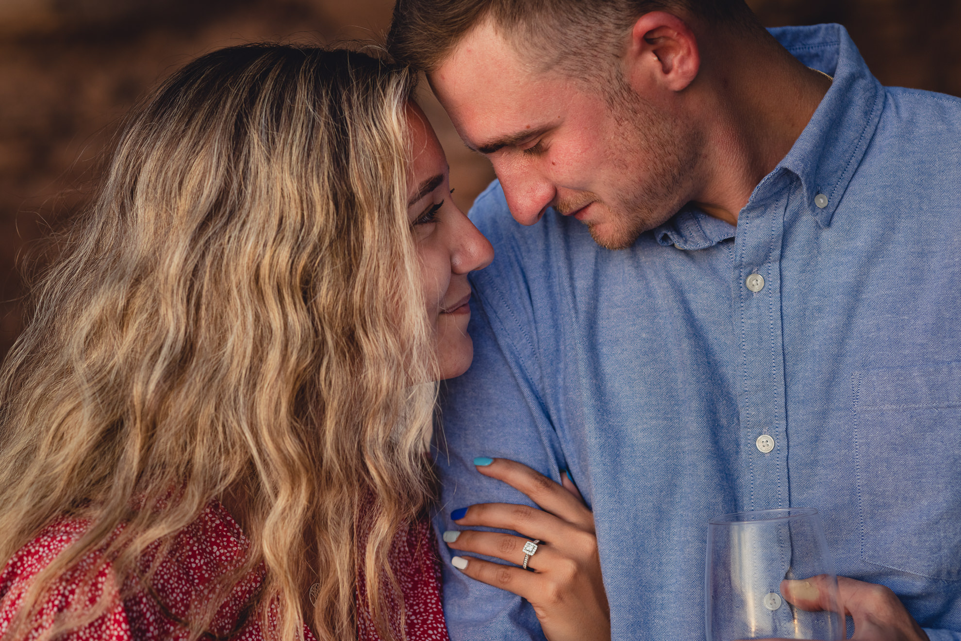 couple drinks wine after proposal on Lake Ontario beach at sunset during wedding engagement proposal photography in Niagara County