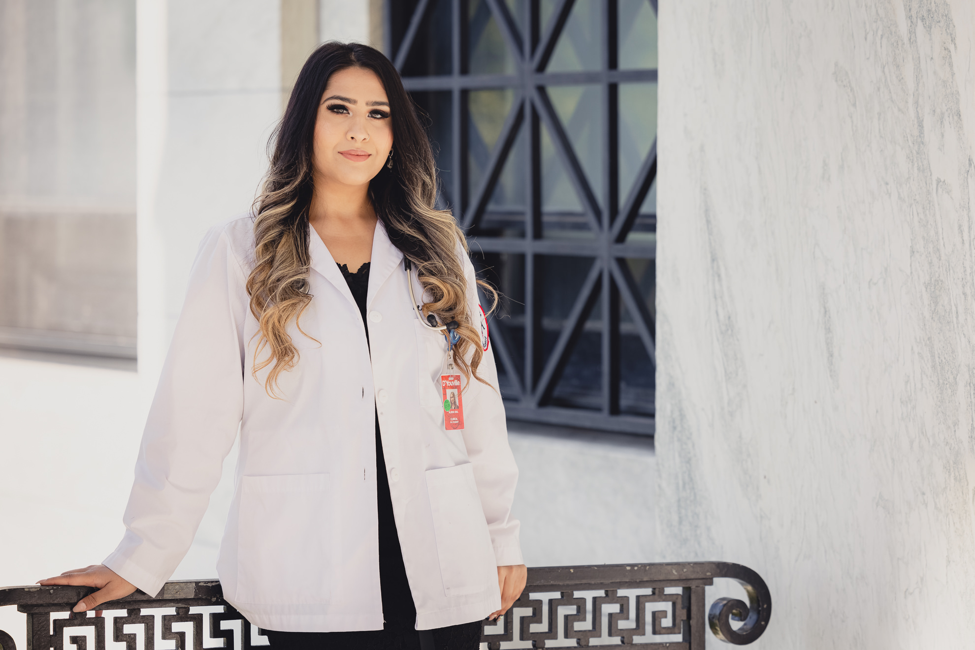 graduate smiles for photographer in D'Youville College white coat during senior graduation portrait photography at the History Museum in Buffalo, NY