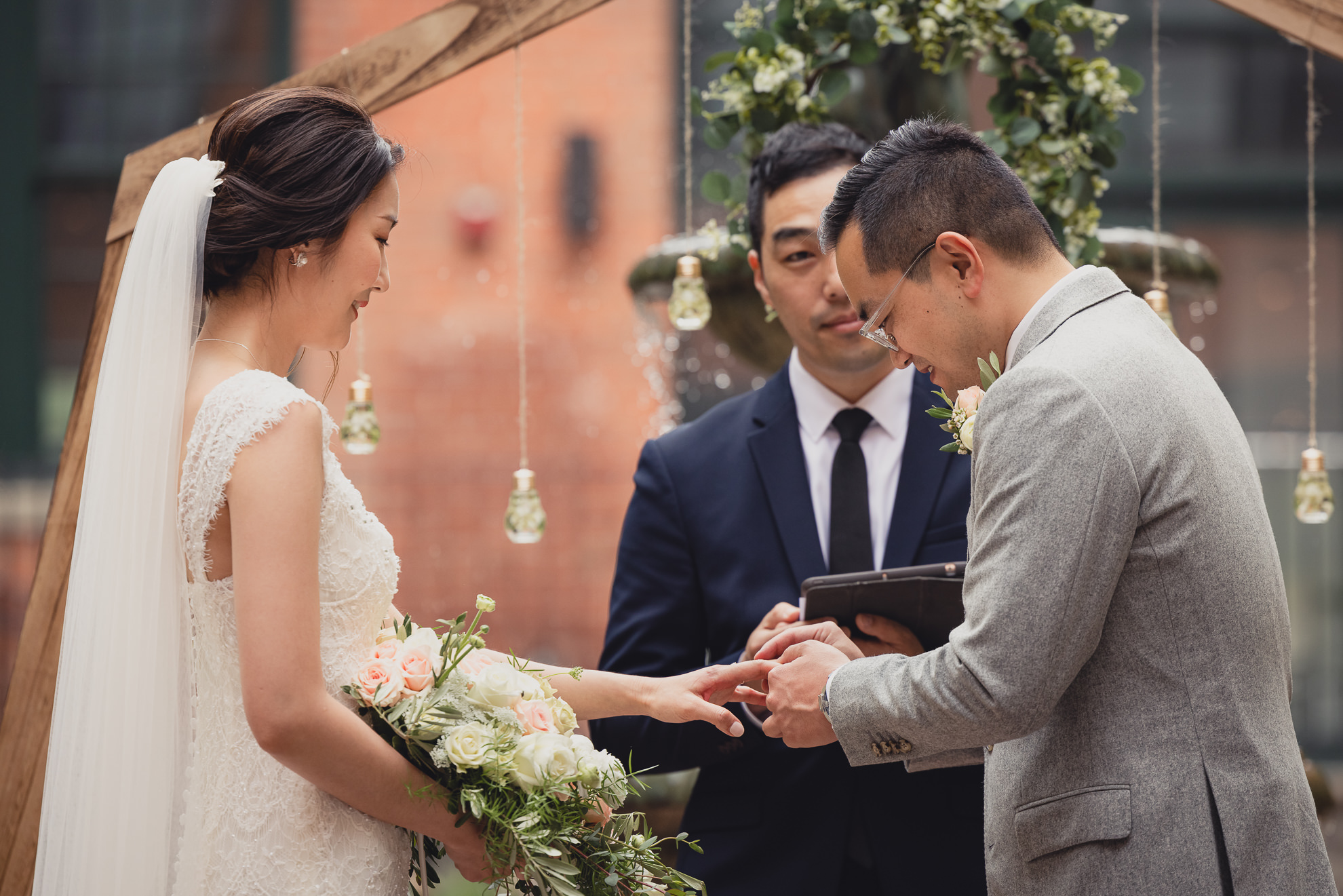 groom places ring on brides finger during wedding ceremony at the Foundry Suites in Buffalo, NY