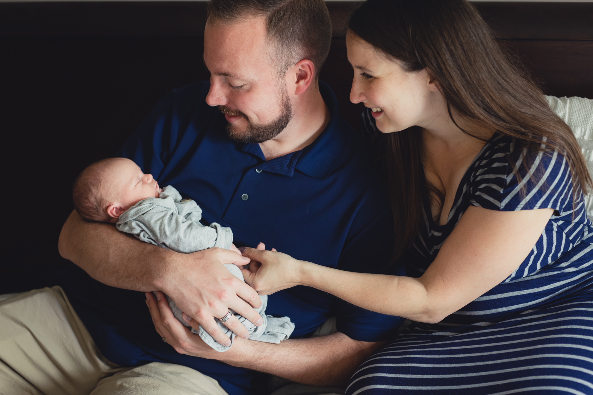 mom and dad look at new baby while sitting on bed during newborn baby family photography session in Buffalo, NY