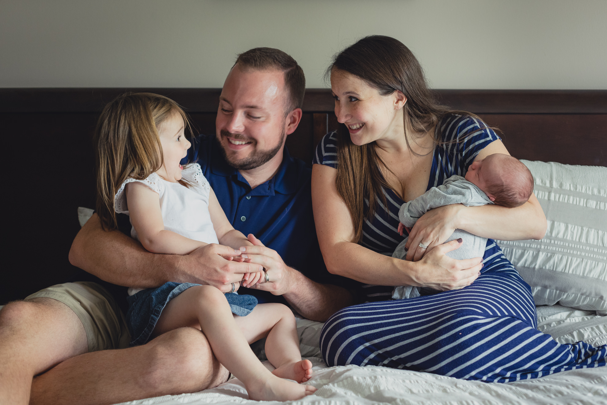 family laughs together while sitting on bed during newborn baby family photography session in Buffalo, NY