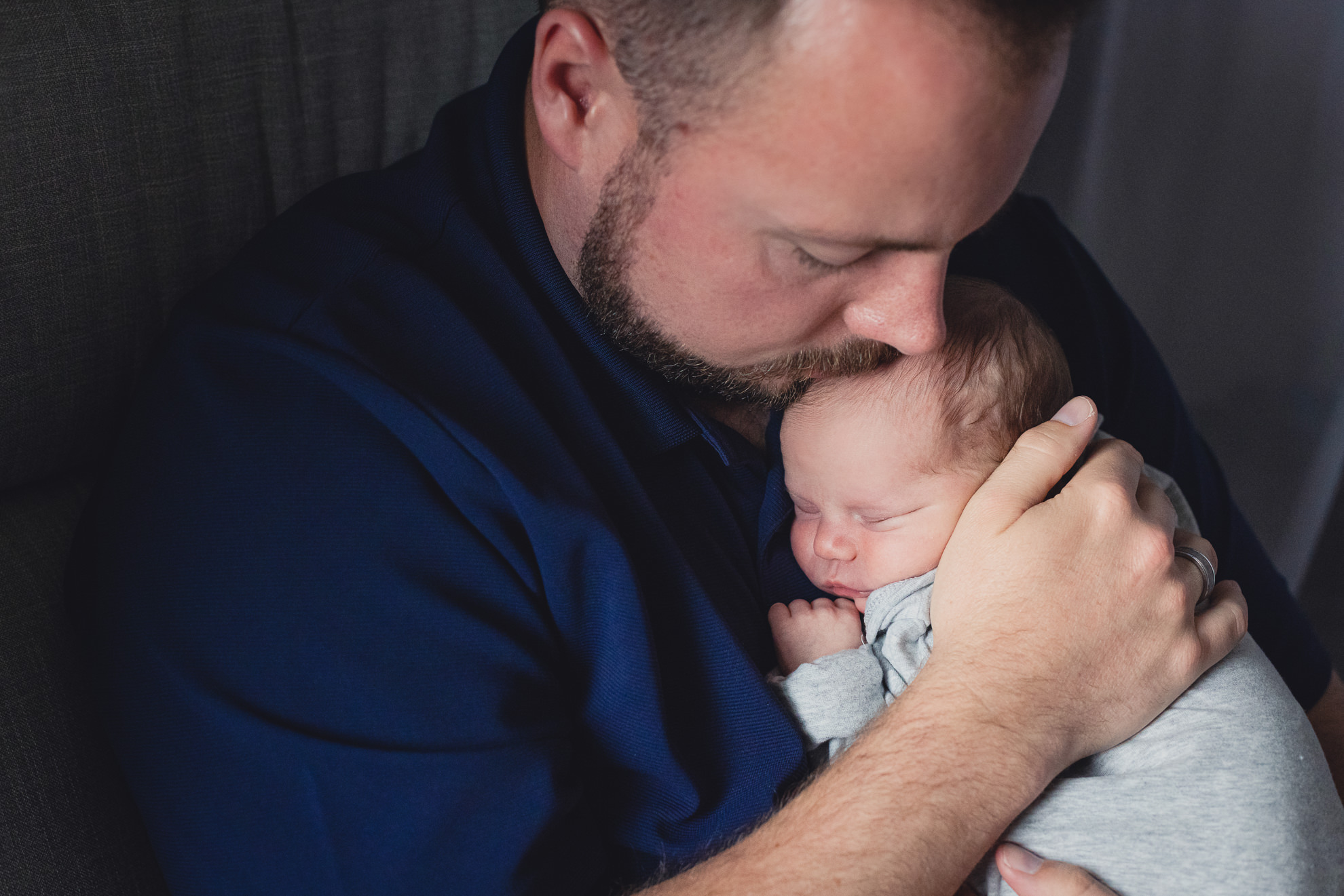 dad kisses babies head while sitting on chair during newborn baby family photography session in Buffalo, NY
