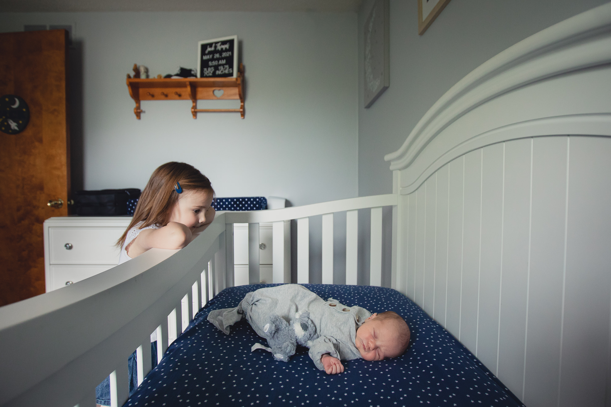 big sister looks at baby in crib during newborn baby family photography session in Buffalo, NY