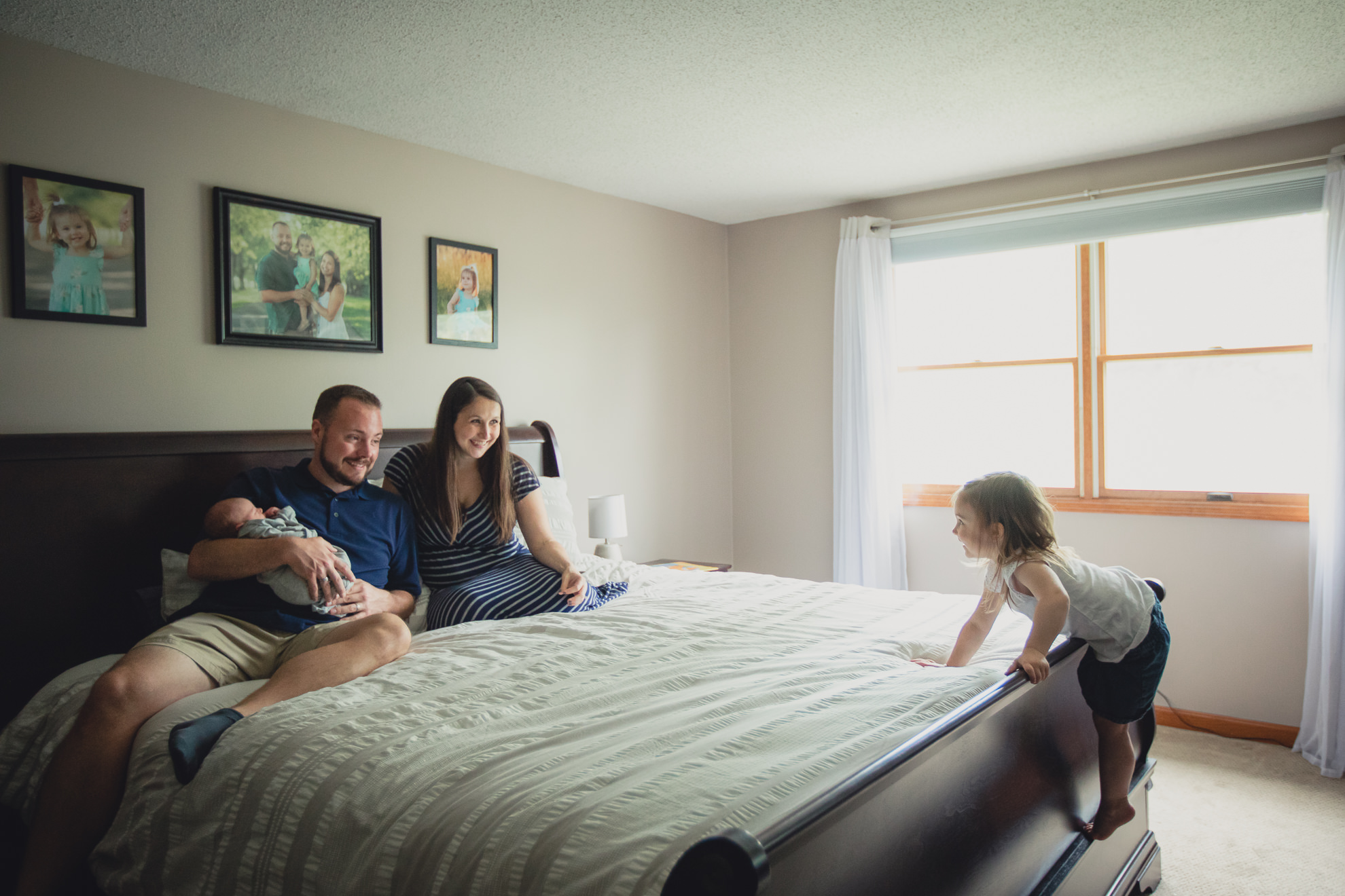 family sits on bed during newborn baby family photography session in Buffalo, NY