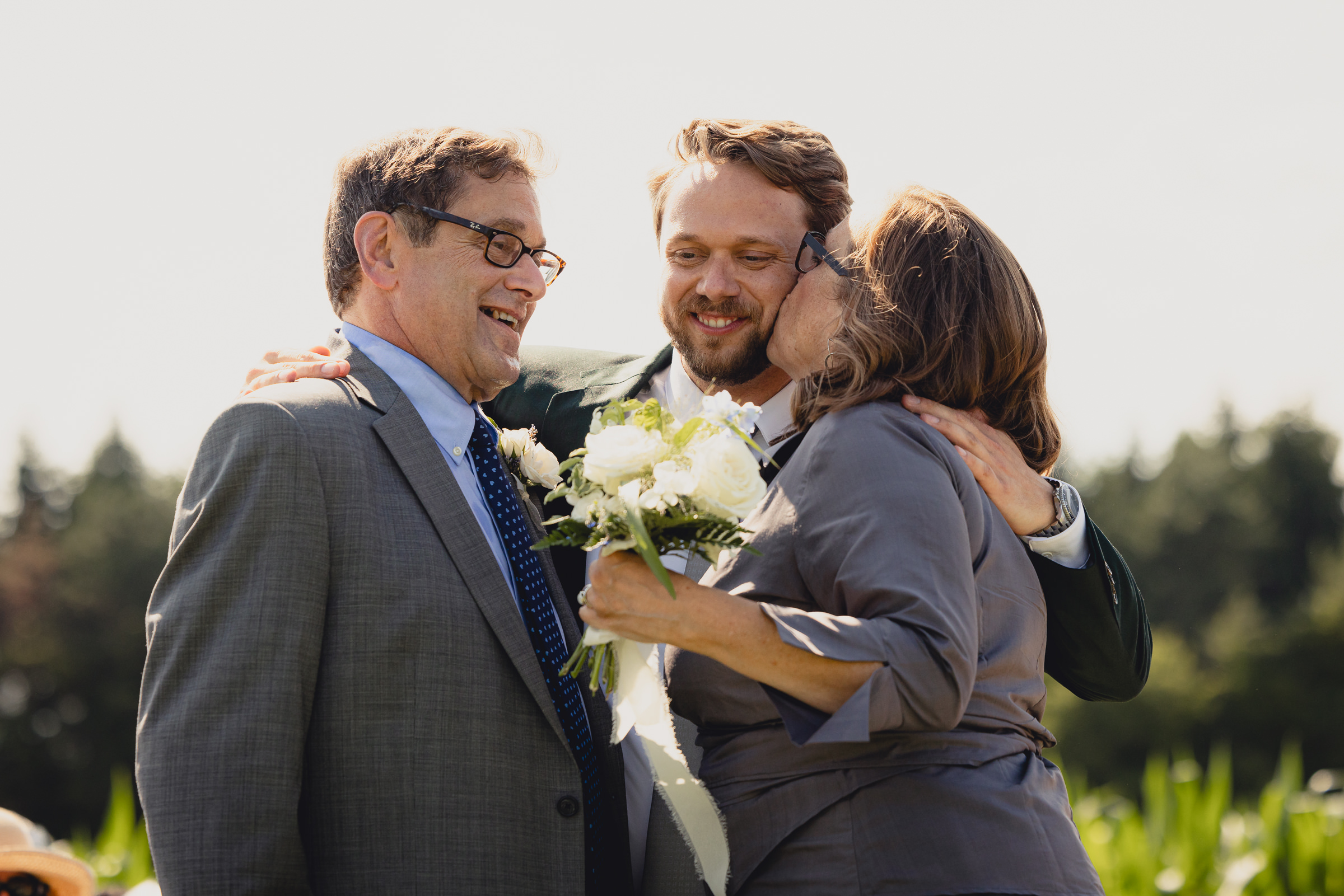 mom kisses grooms cheek at wedding ceremony at The North Farm overlooking Seneca Lake in Geneva, NY