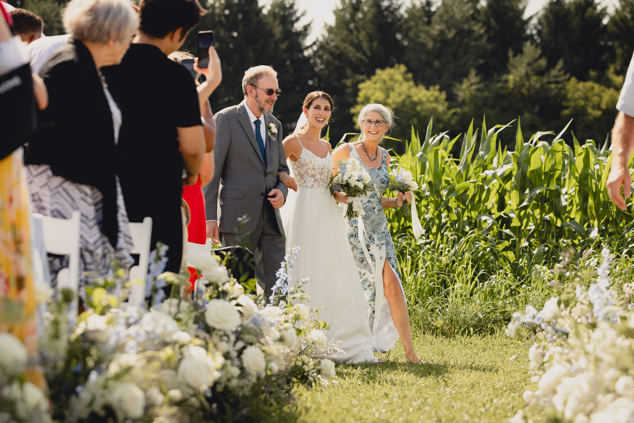bride walks down aisle with parents at wedding ceremony at The North Farm overlooking Seneca Lake in Geneva, NY