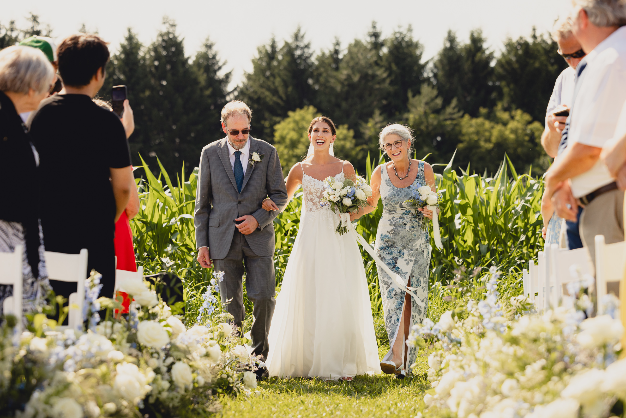 bride walks down aisle with parents at wedding ceremony at The North Farm overlooking Seneca Lake in Geneva, NY