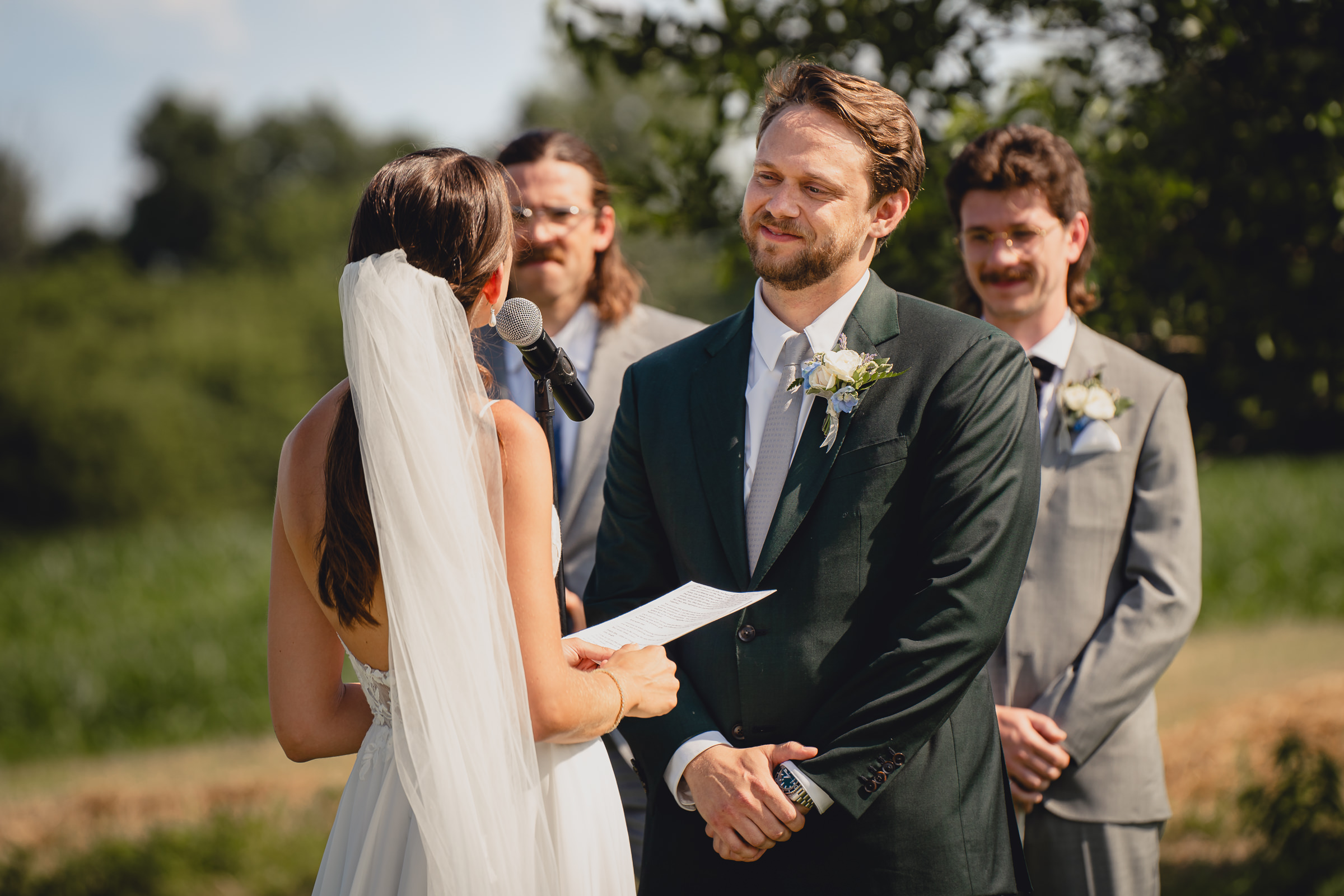 groom smiles at bride at wedding ceremony at The North Farm overlooking Seneca Lake in Geneva, NY