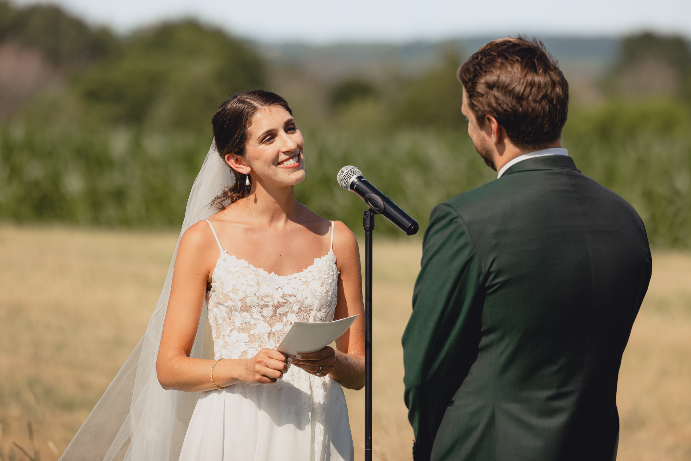 bride smiles at groom at wedding ceremony at The North Farm overlooking Seneca Lake in Geneva, NY