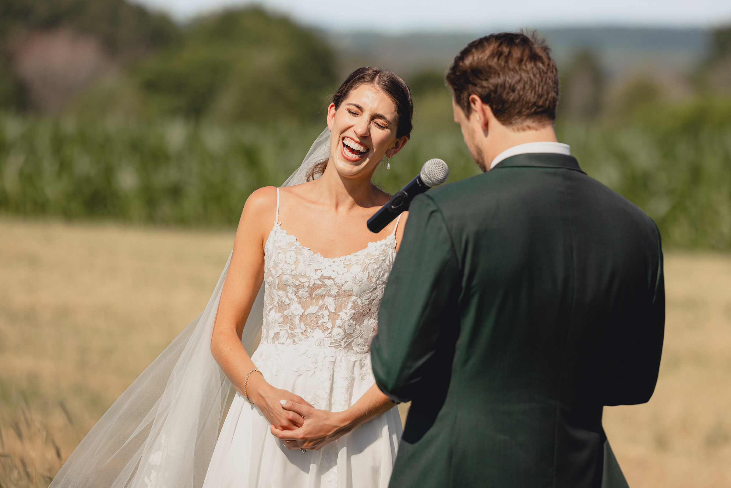 bride laughs while groom says vows at wedding ceremony at The North Farm overlooking Seneca Lake in Geneva, NY