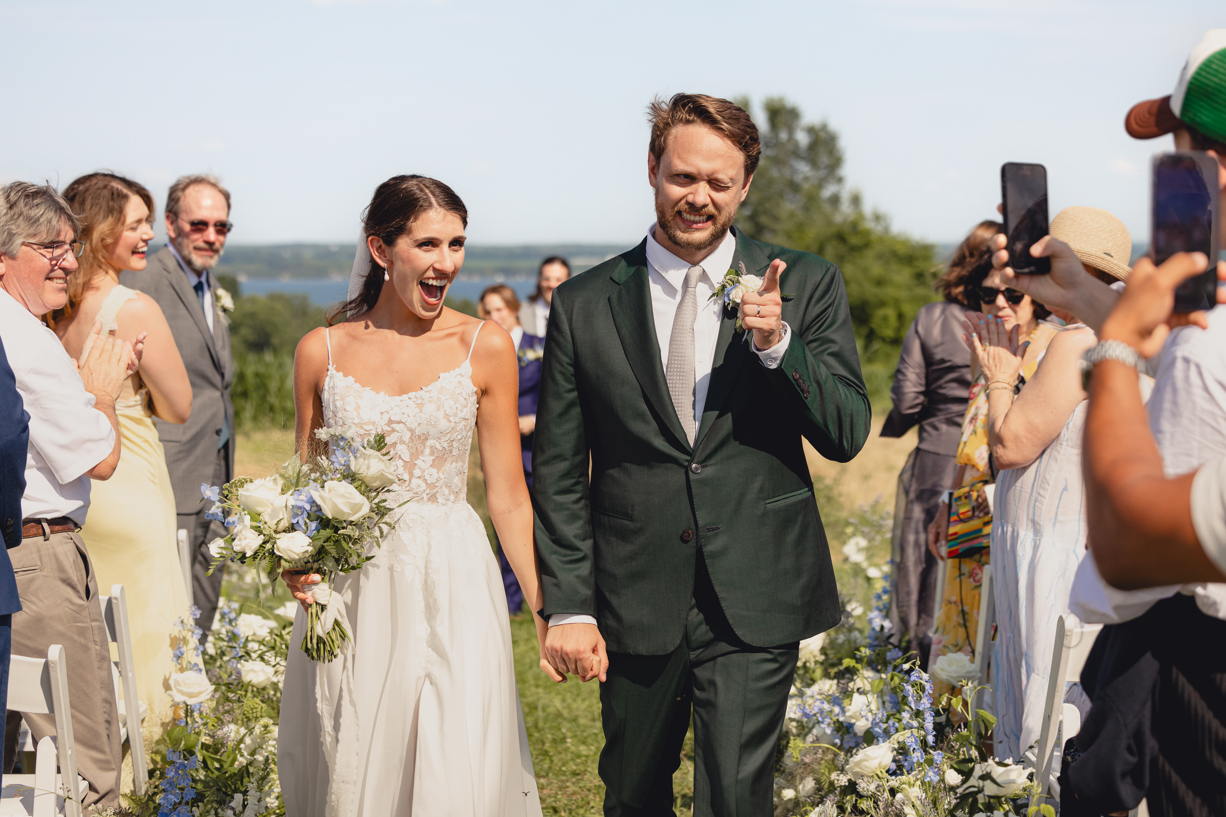 bride and groom walk down aisle  and groom winks after wedding ceremony at The North Farm overlooking Seneca Lake in Geneva, NY