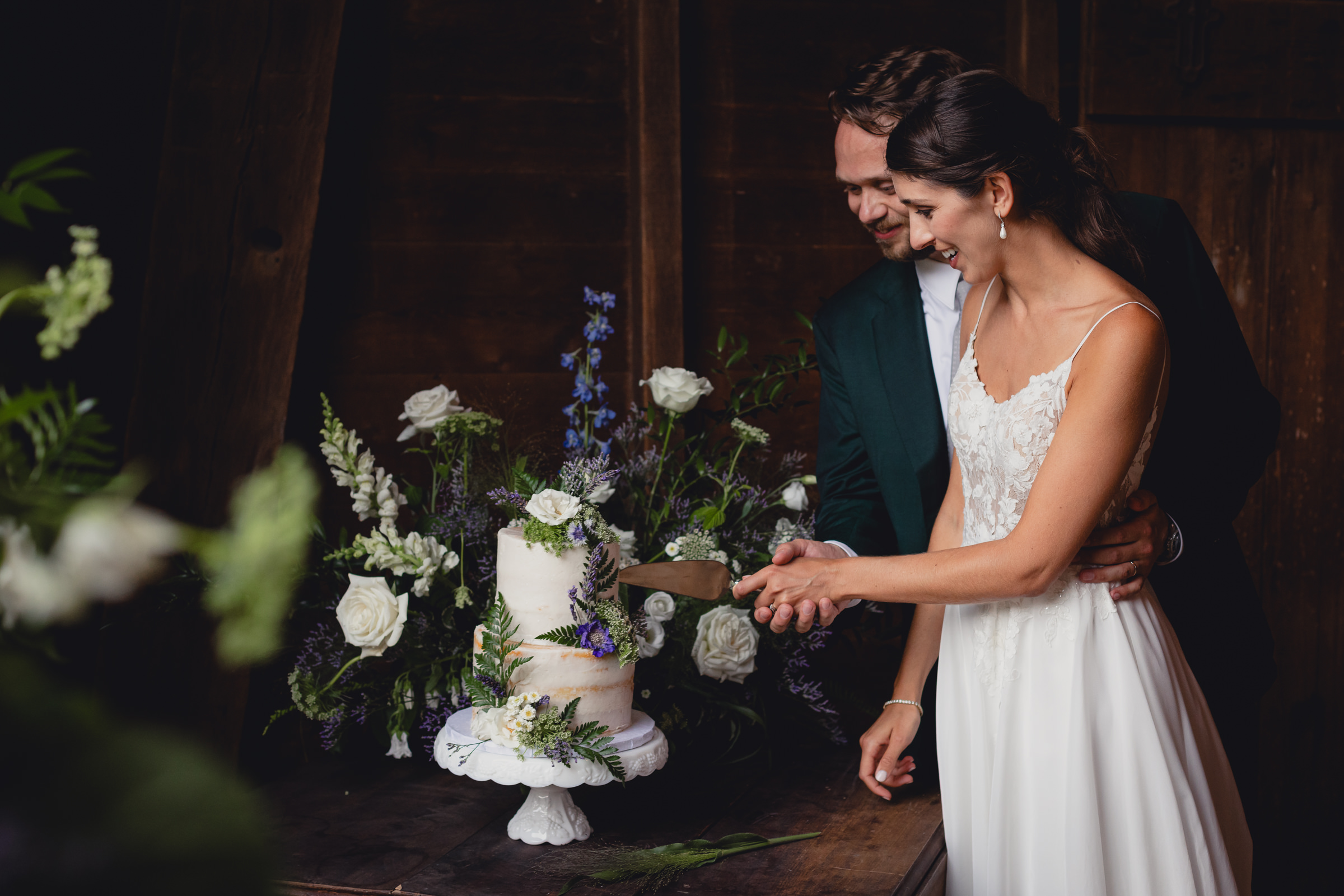 bride and groom cut cake at wedding reception in barn at The North Farm in Geneva, NY