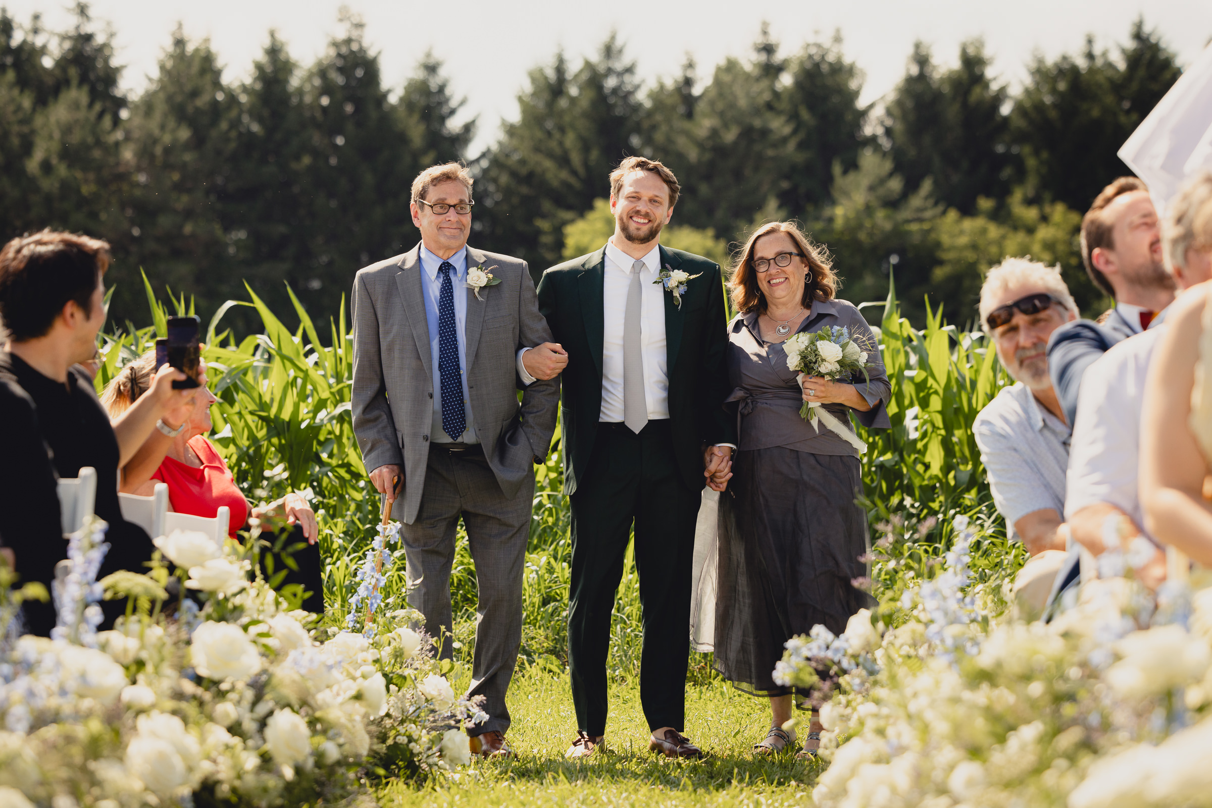groom walks down aisle with parents at wedding ceremony at The North Farm overlooking Seneca Lake in Geneva, NY