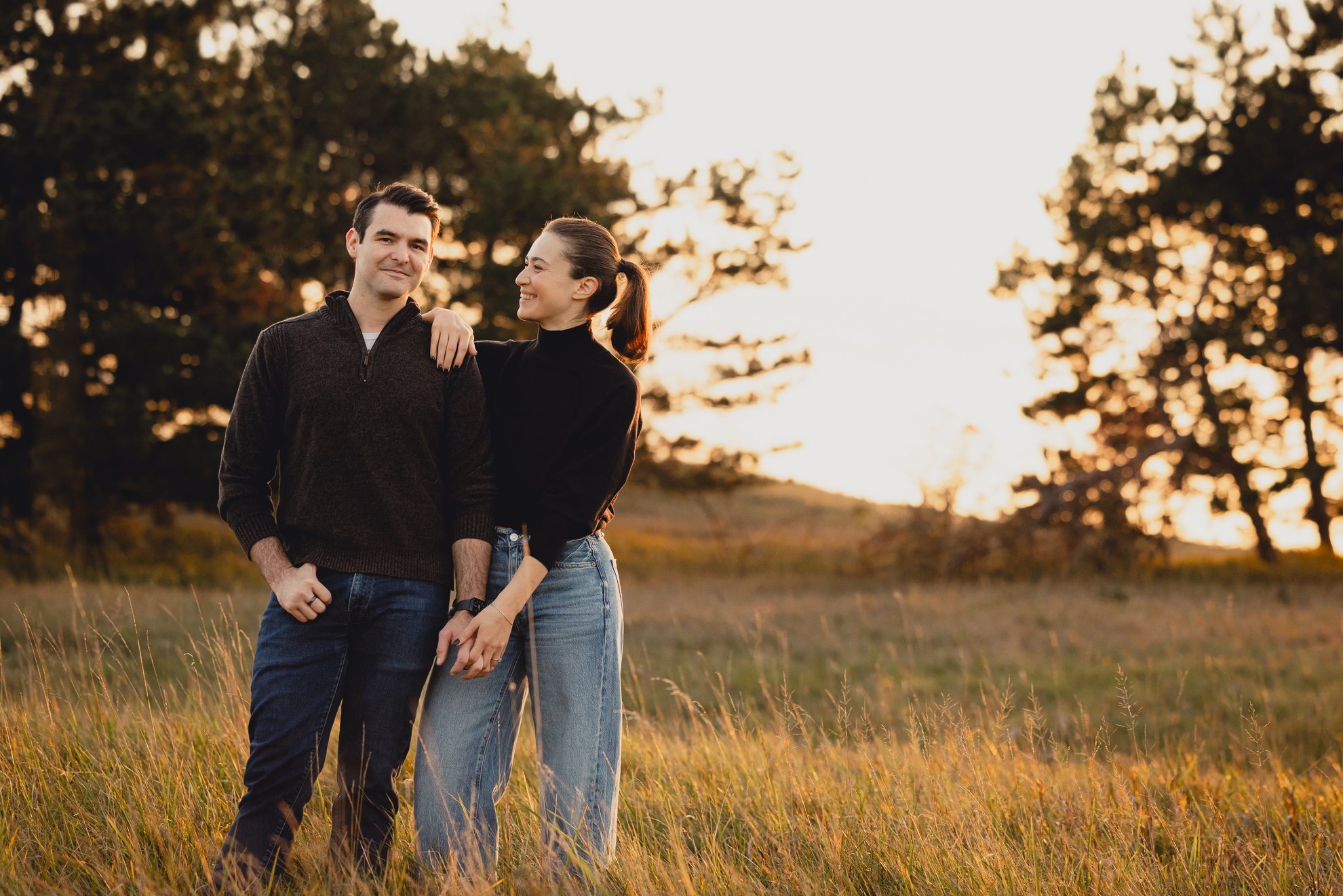 couple stands and laughs in field at Tifft Natre Preserve at sunset during wedding engagement photos in Buffalo