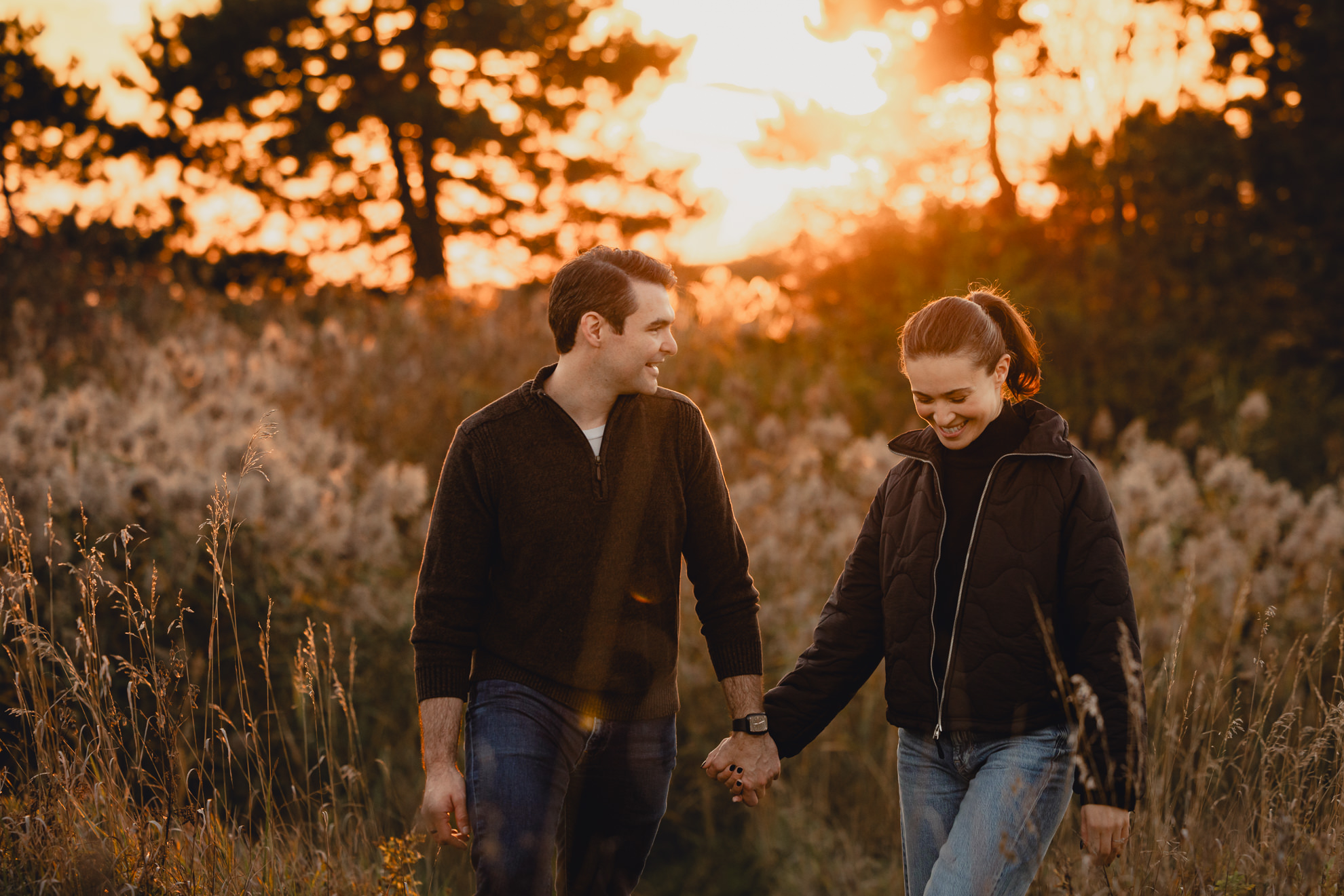 couple holds hands in field at sunset during wedding engagement photos in Buffalo NY