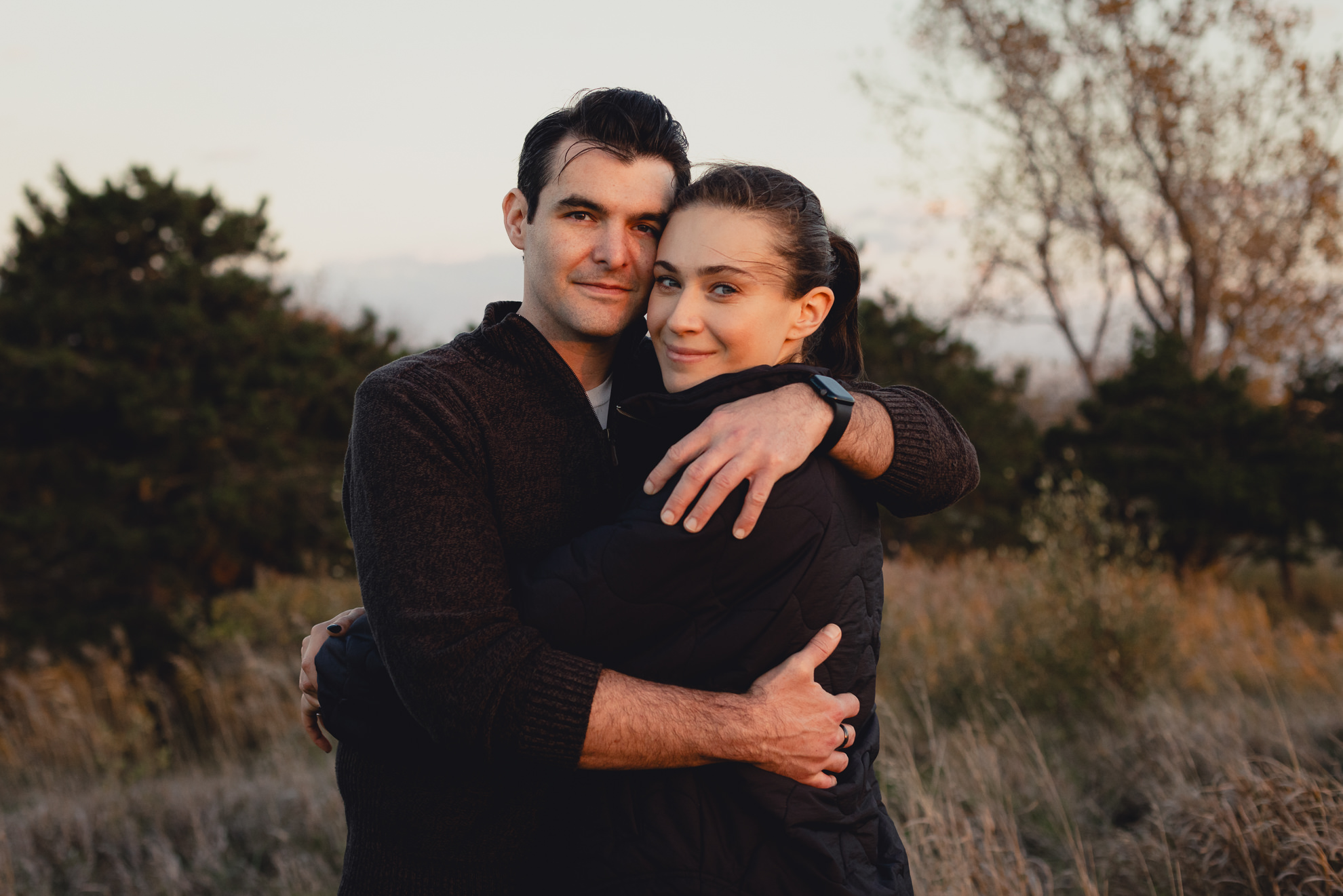 couple emgraces in field at Tifft Natre Preserve at sunset during wedding engagement photos in Buffalo NY