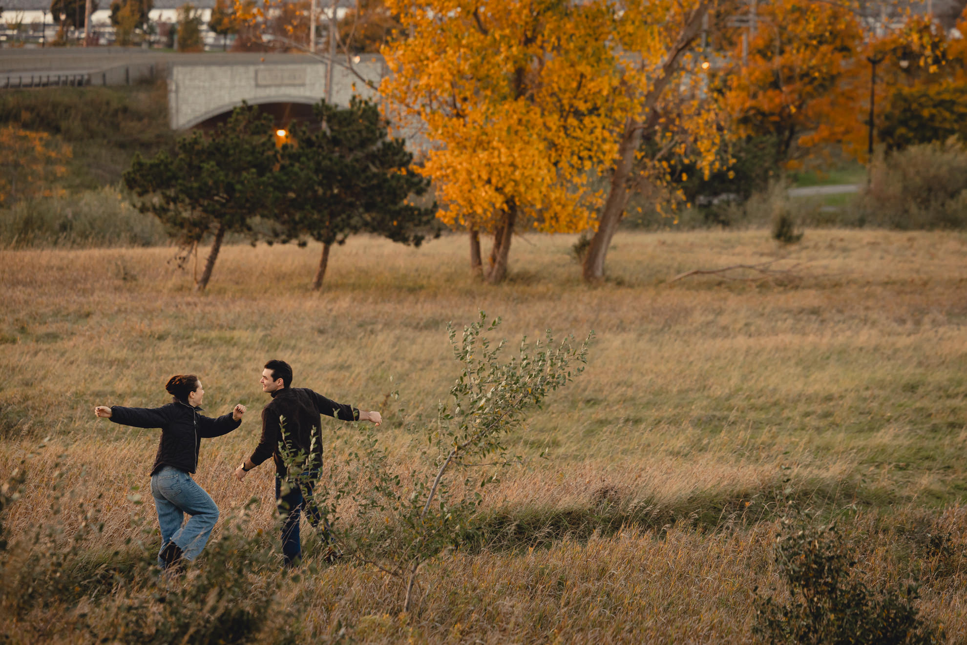 couple skips down path in field at Tifft Natre Preserve at sunset during wedding engagement pictures in Buffalo