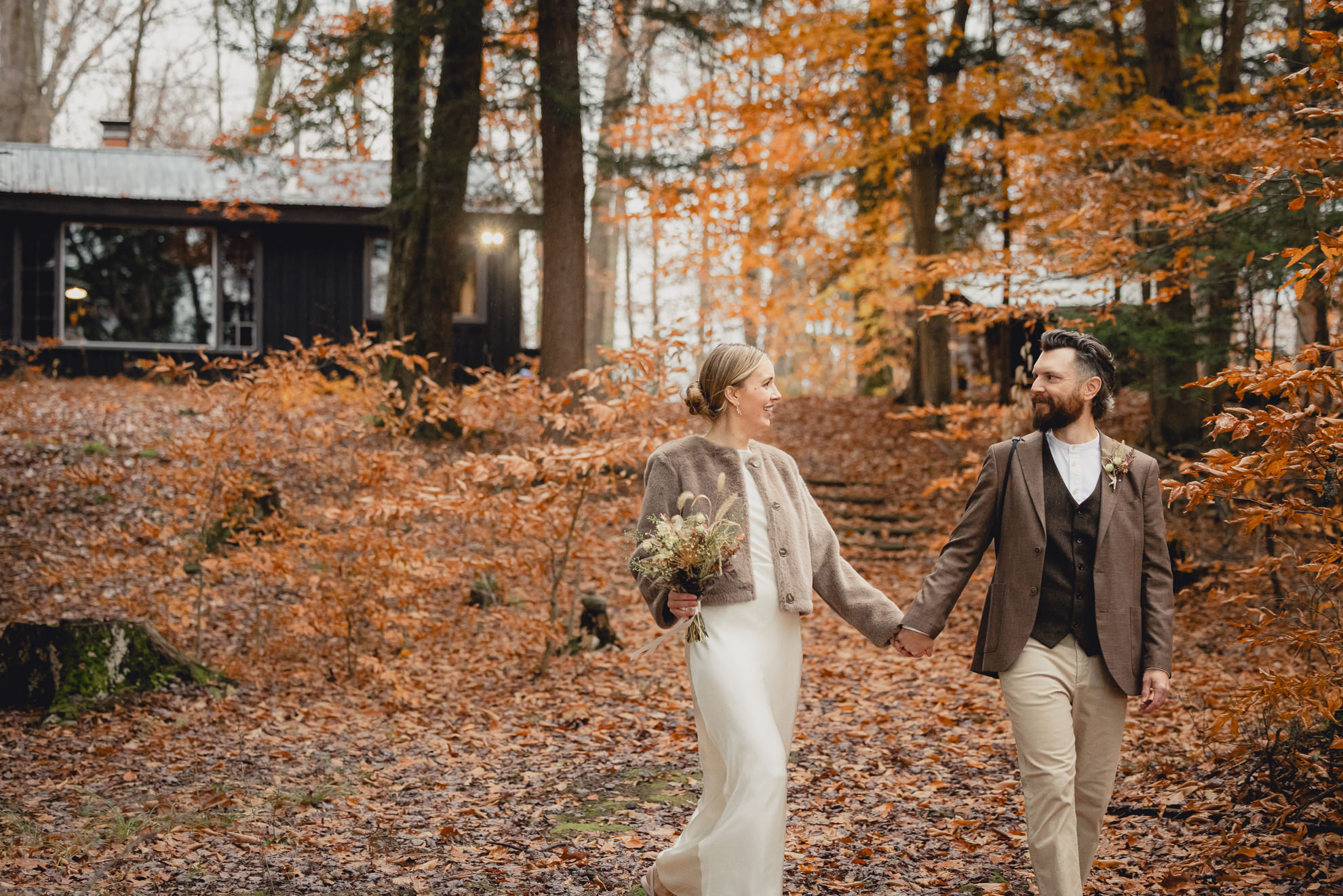 bride and groom look at each other and walk down steps groom photographs bride outside Langston Cottage at Vanderkamp NY before fall wedding in the Adirondacks
