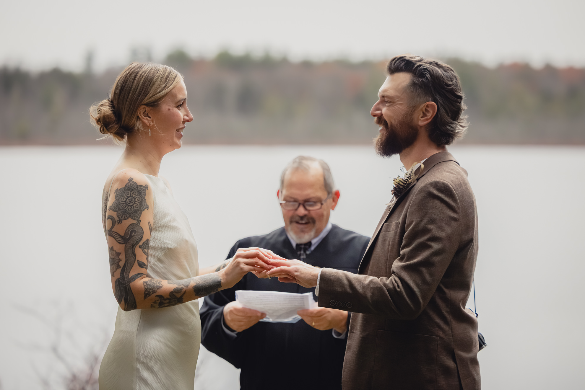 bride and groom look at each other smiling as bride places ring on grooms finger during micro wedding elopement ceremony at Vanderkamp NY in the Adirondacks