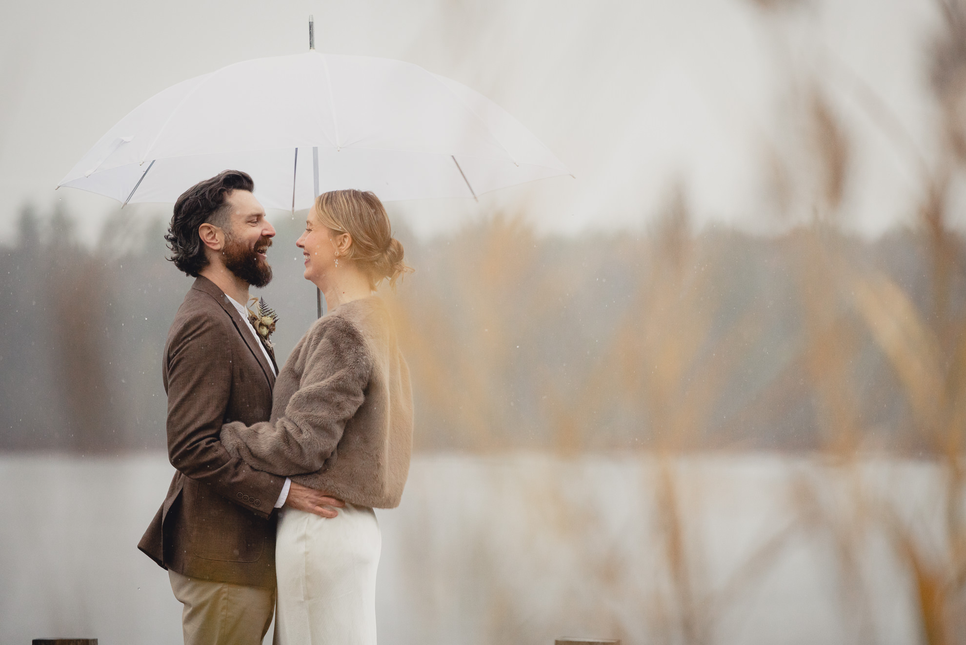 bride and groom laugh with umbrella at lake during fall after micro wedding elopement ceremony at Vanderkamp NY in the Adirondacks