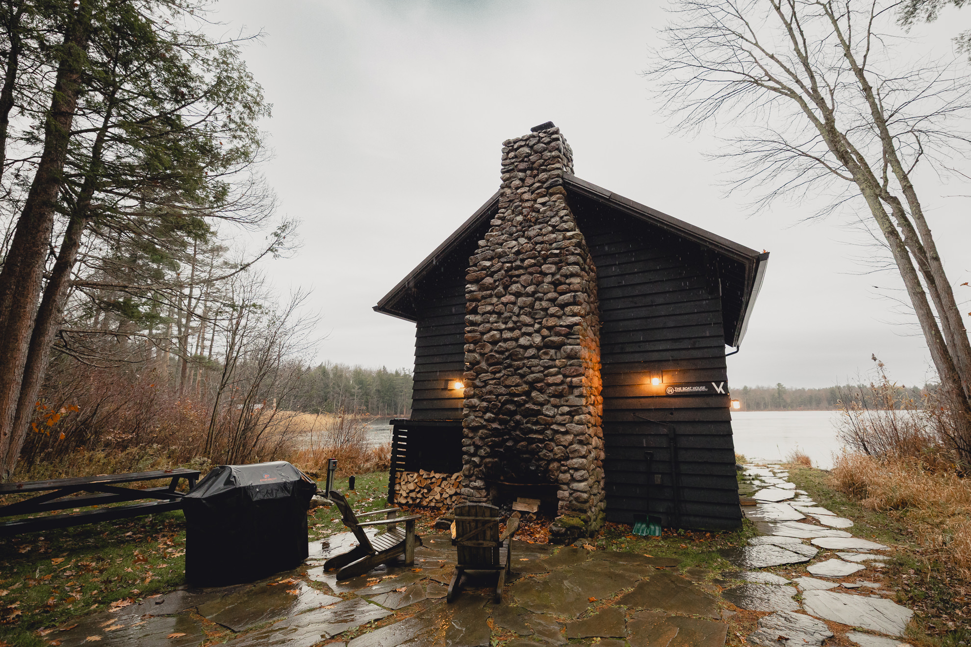 The boathouse is pictured in rain by lake during fall after micro wedding elopement at Vanderkamp NY in the Adirondacks