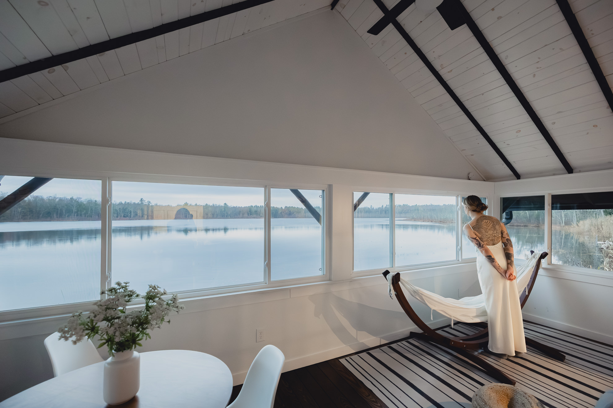 bride looks out at lake from boathouse during fall after micro wedding elopement at Vanderkamp NY in the Adirondacks